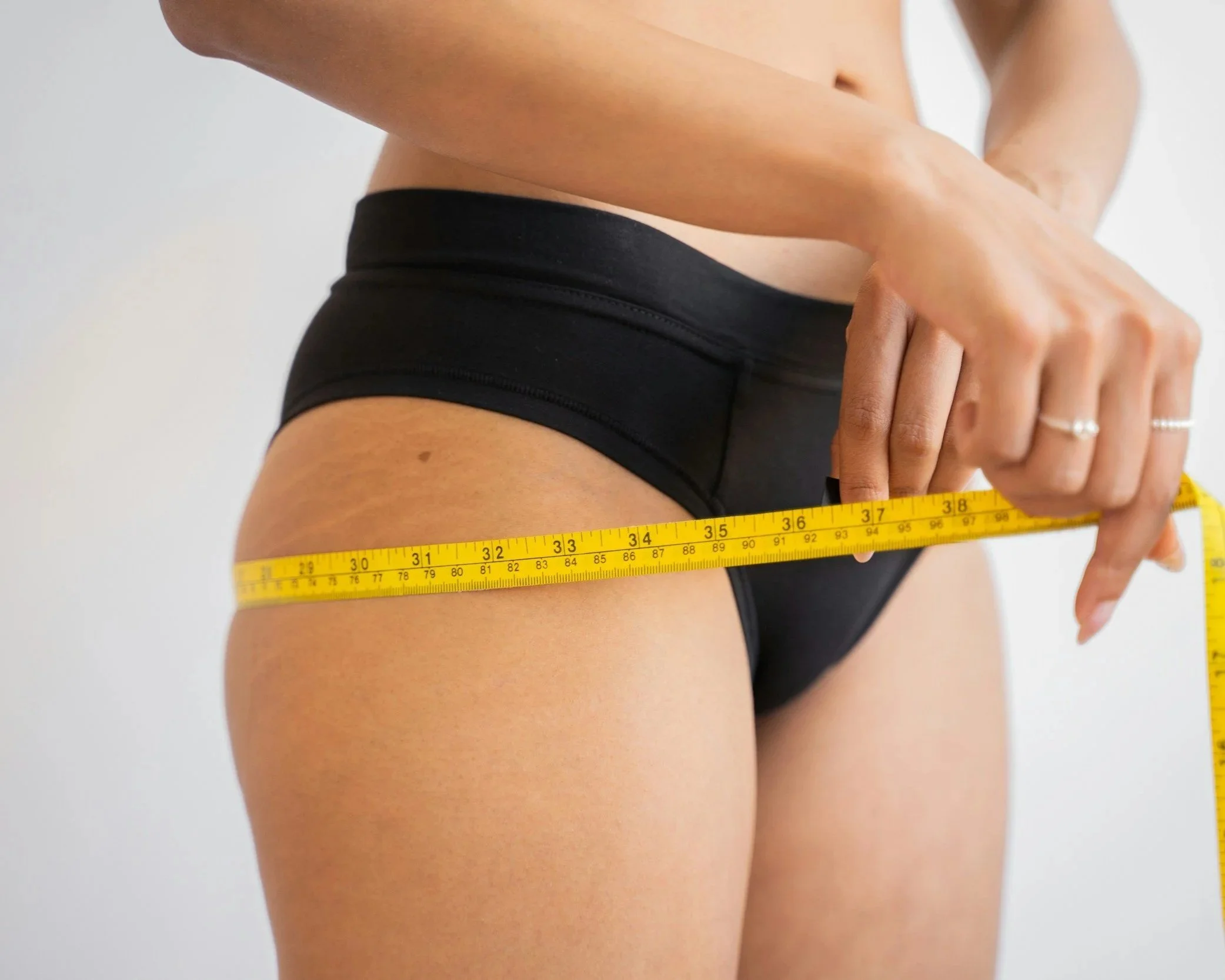 A person measuring their waist with a yellow tape measure.