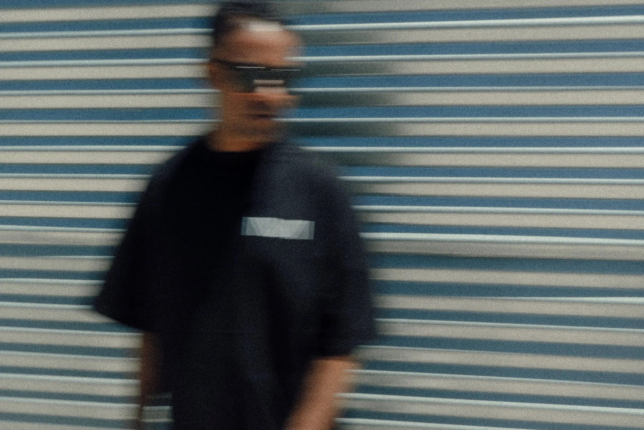 Person with glasses holding a smartphone standing in front of a horizontally striped background, with motion blur.