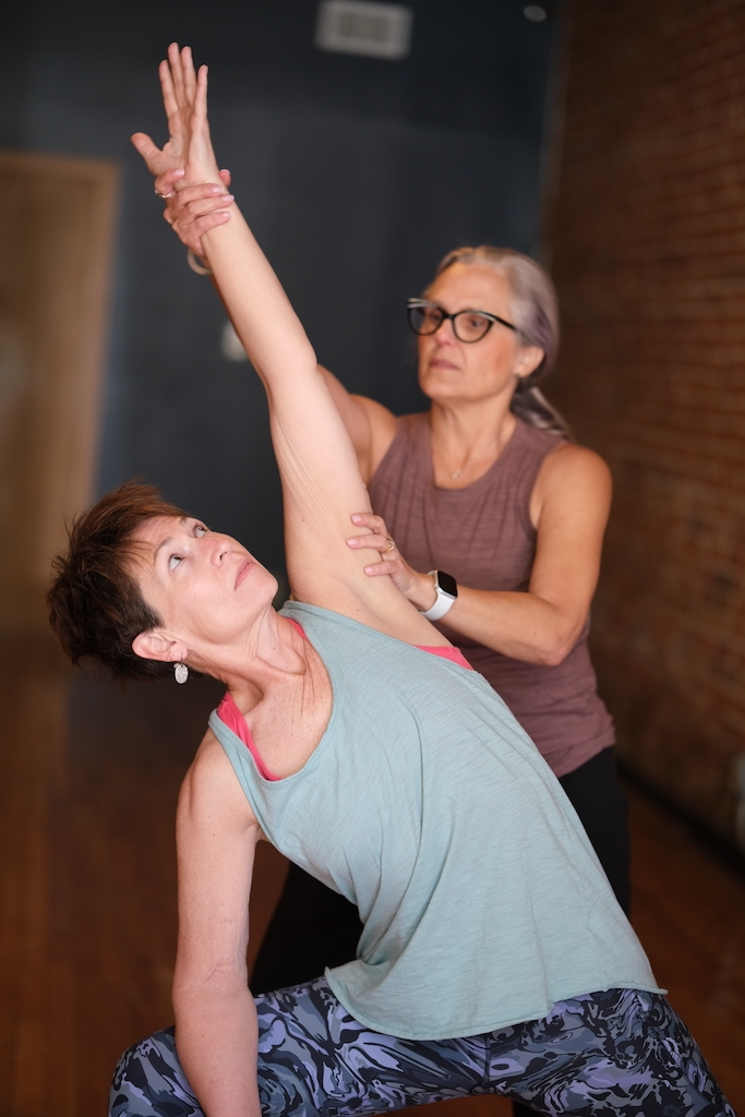 An elderly woman practicing yoga with assistance from an instructor in a studio.