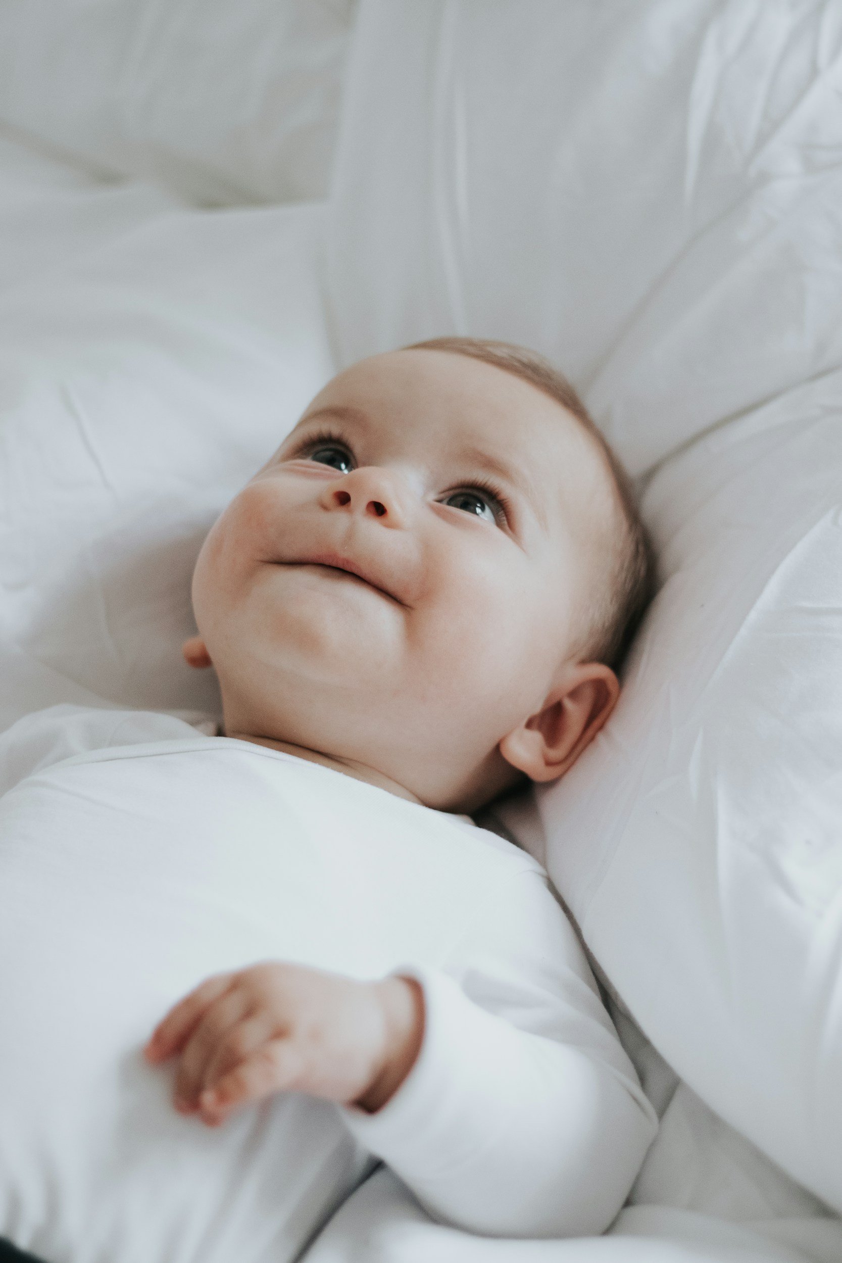 Happy baby lying on a white blanket representing pediatric wellness care for infants at Moms & Minis Wellness Co. in Brevard County, FL.