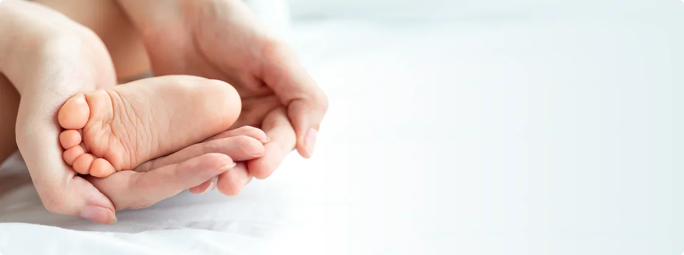 A close-up of an adult's hand holding a baby's foot with tiny toes, resting on a white surface.