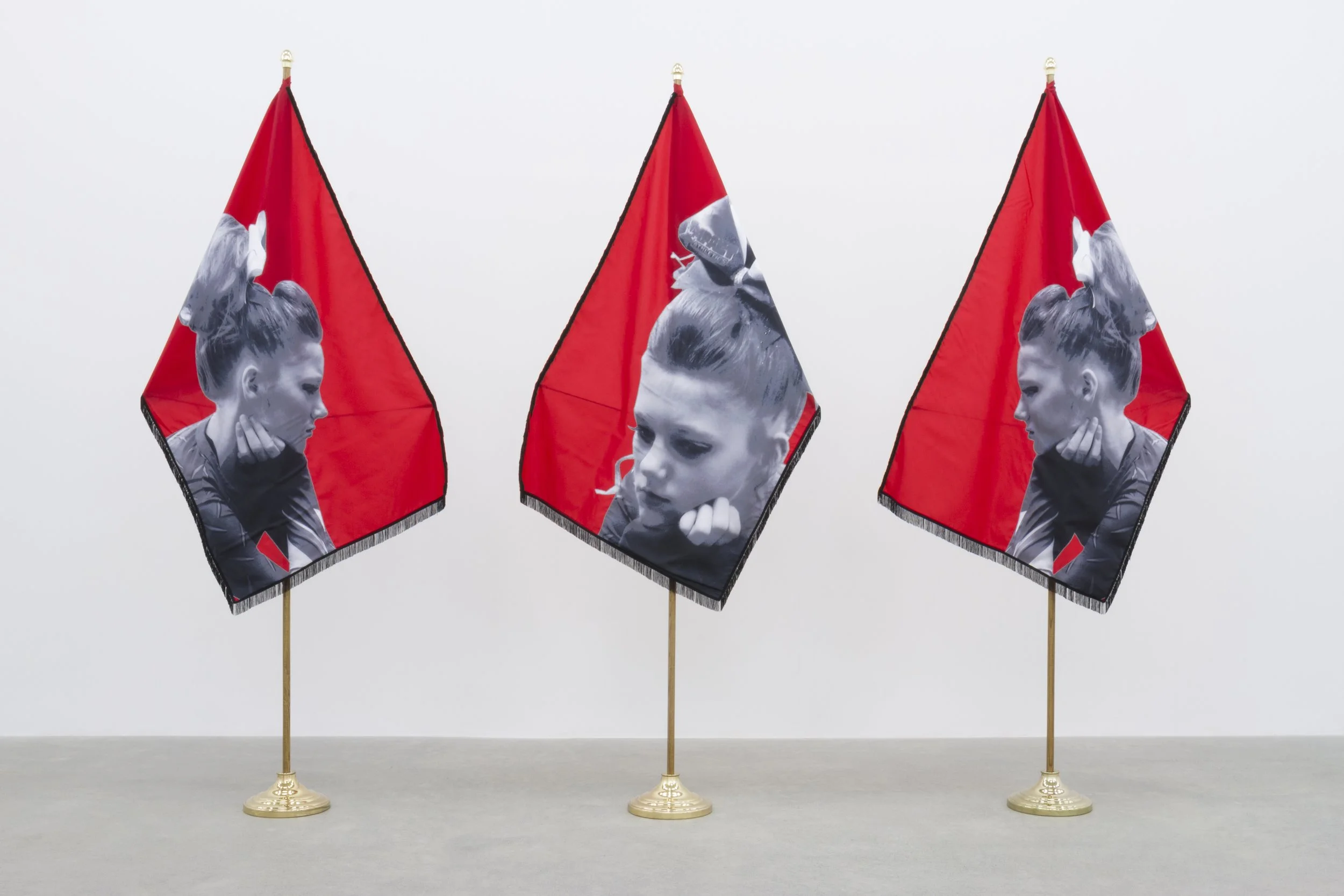 Three flags with grayscale images of a girl with her hair in an updo, each flag on a golden flagpole set against a plain white background.