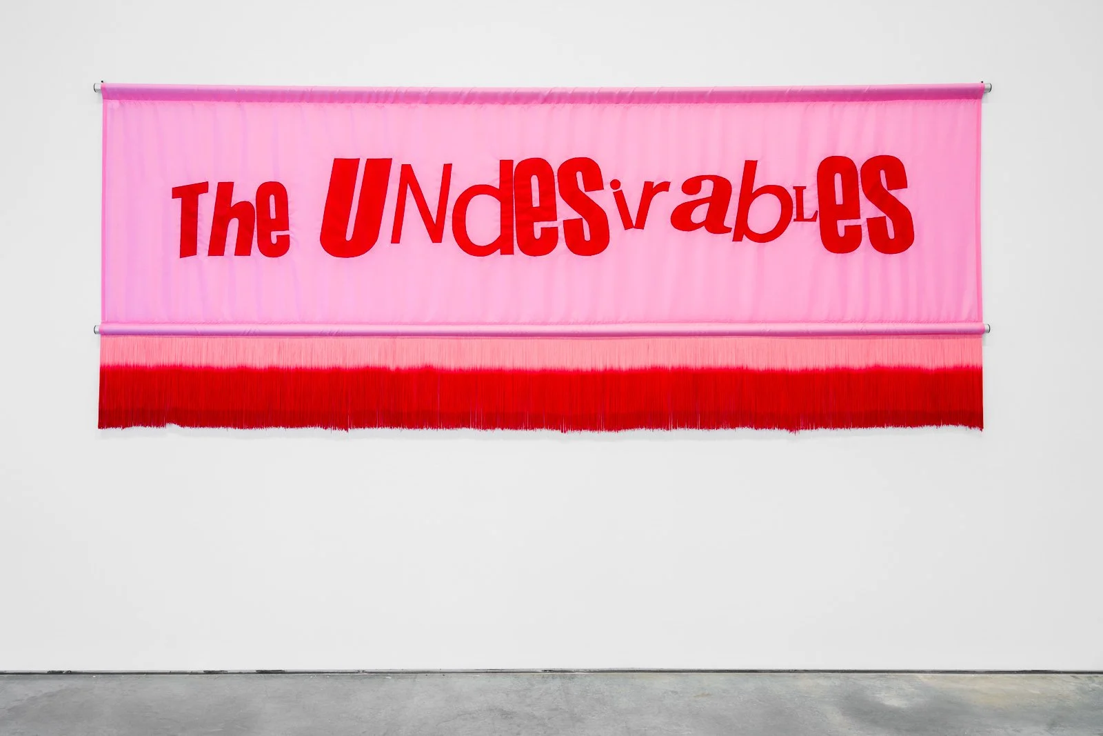 Pink fabric banner with red text reading 'The Undesirables' hanging on a wall.