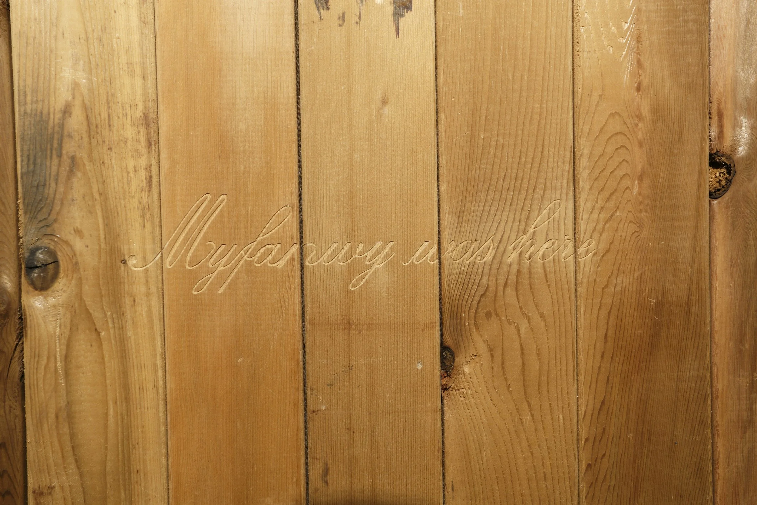 Close-up view of wooden planks with engraved cursive text reading "Maybury is back."
