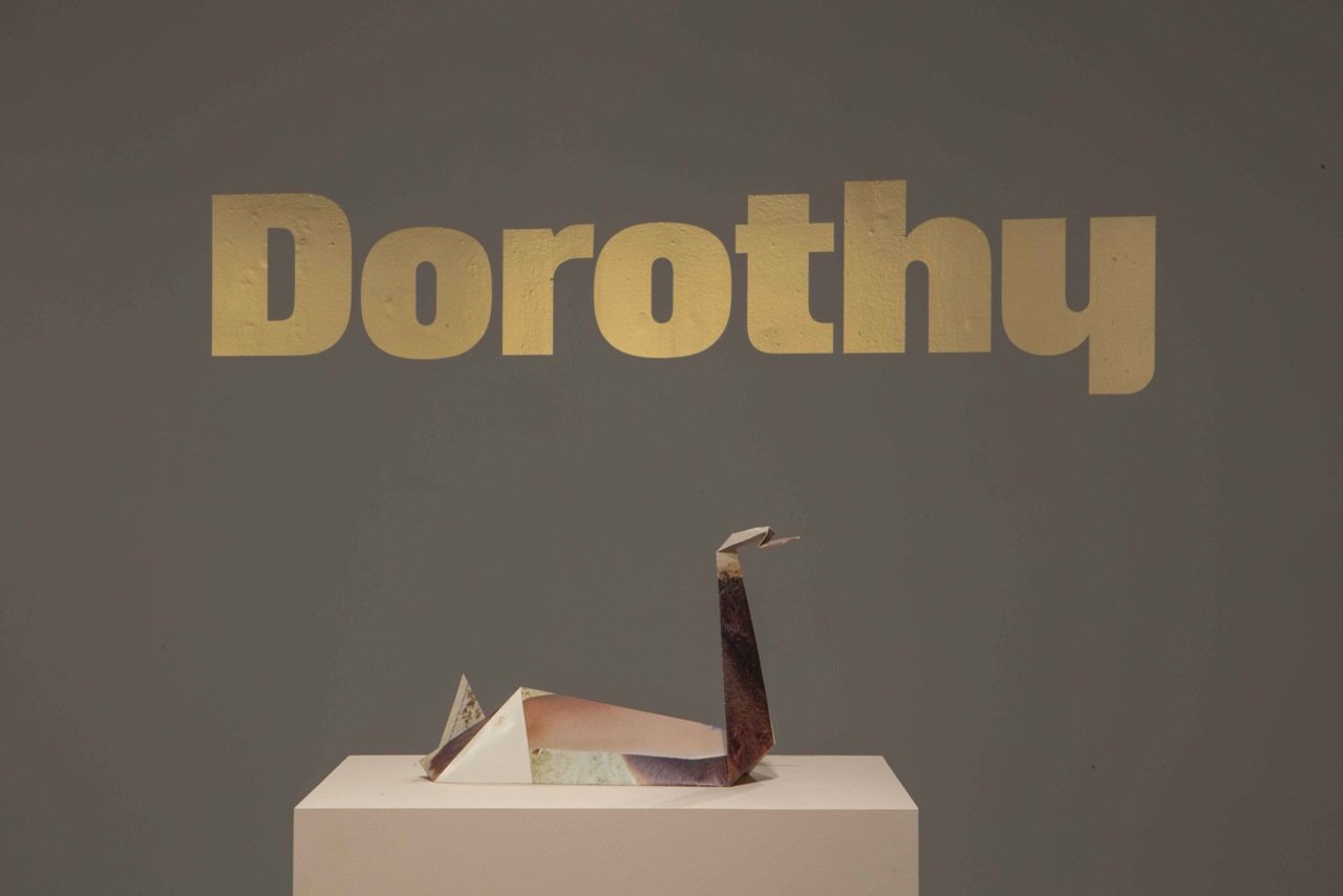A paper origami sculpture of a swan on a display pedestal with the word 'Dorothy' written above it.