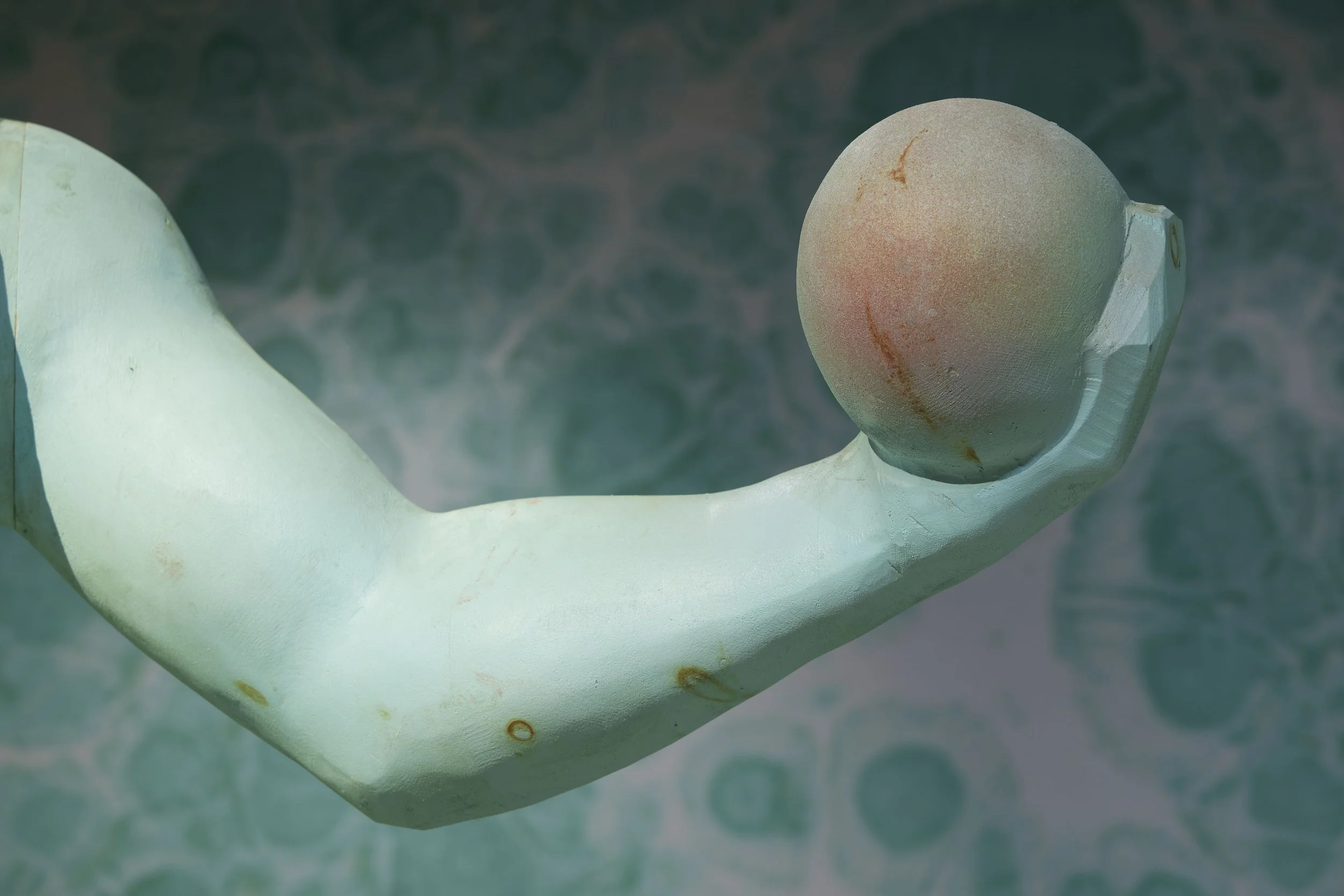 Close-up of a wooden sculpture of a human figure holding an apple, with a marbled background.