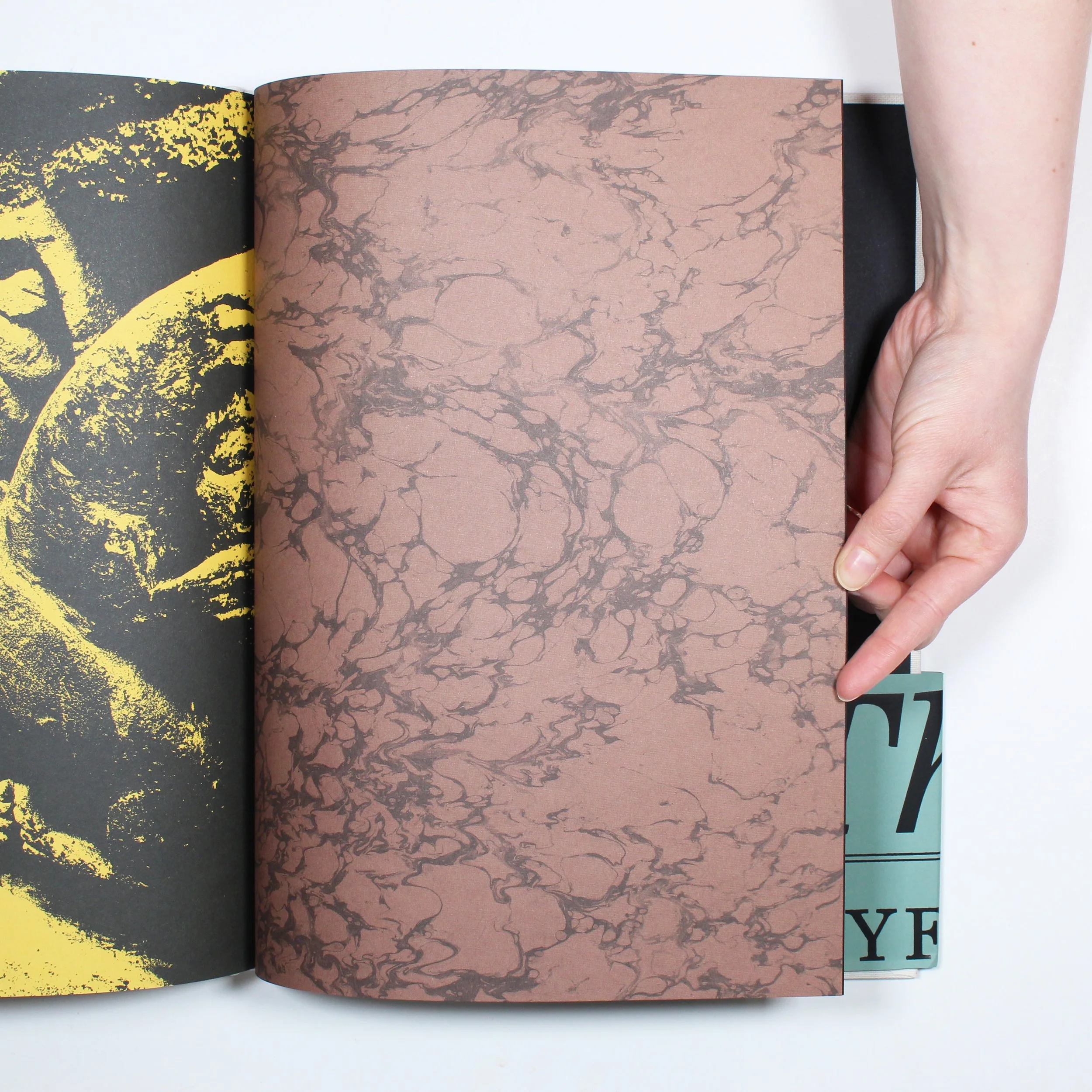 Close-up of an open book with abstract, marbled patterns on the pages and part of a colorful lettered side panel visible.