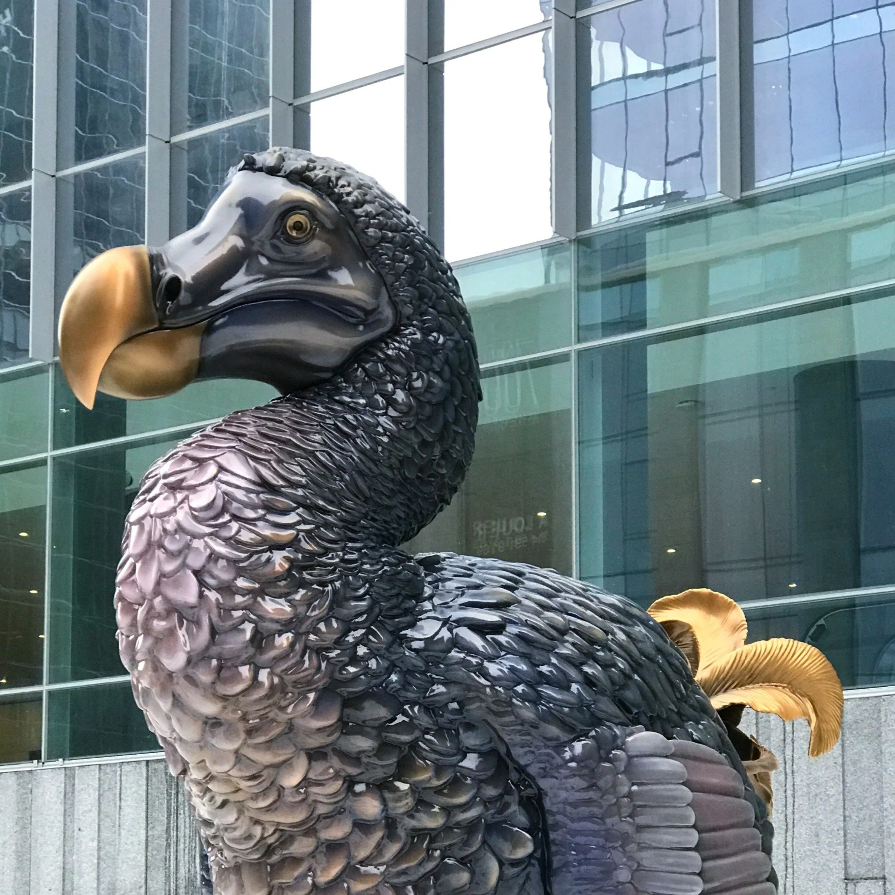 Close-up of a black eagle sculpture with detailed feathers, gold beak, and glass building reflections in the background.