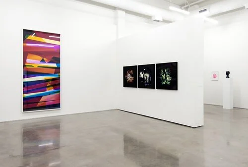 Art gallery with large colorful abstract painting on the left and three smaller black and white photographs on a white wall.