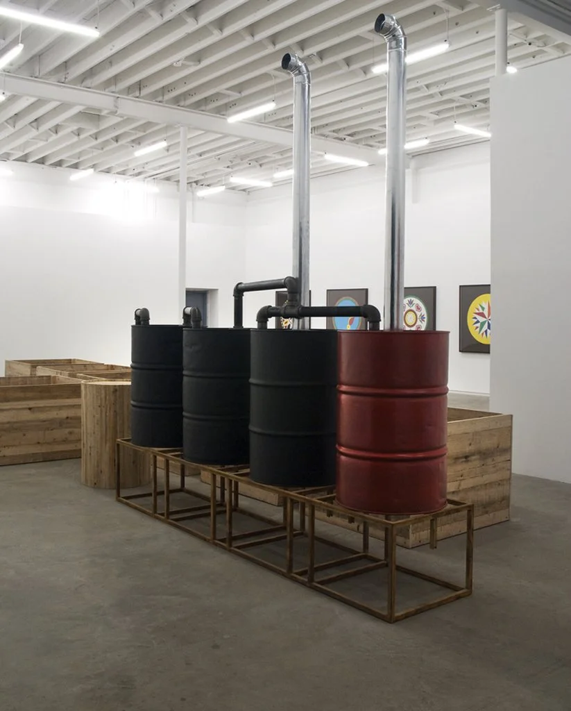 Three large metal barrels connected to pipes in an art gallery or exhibit space.
