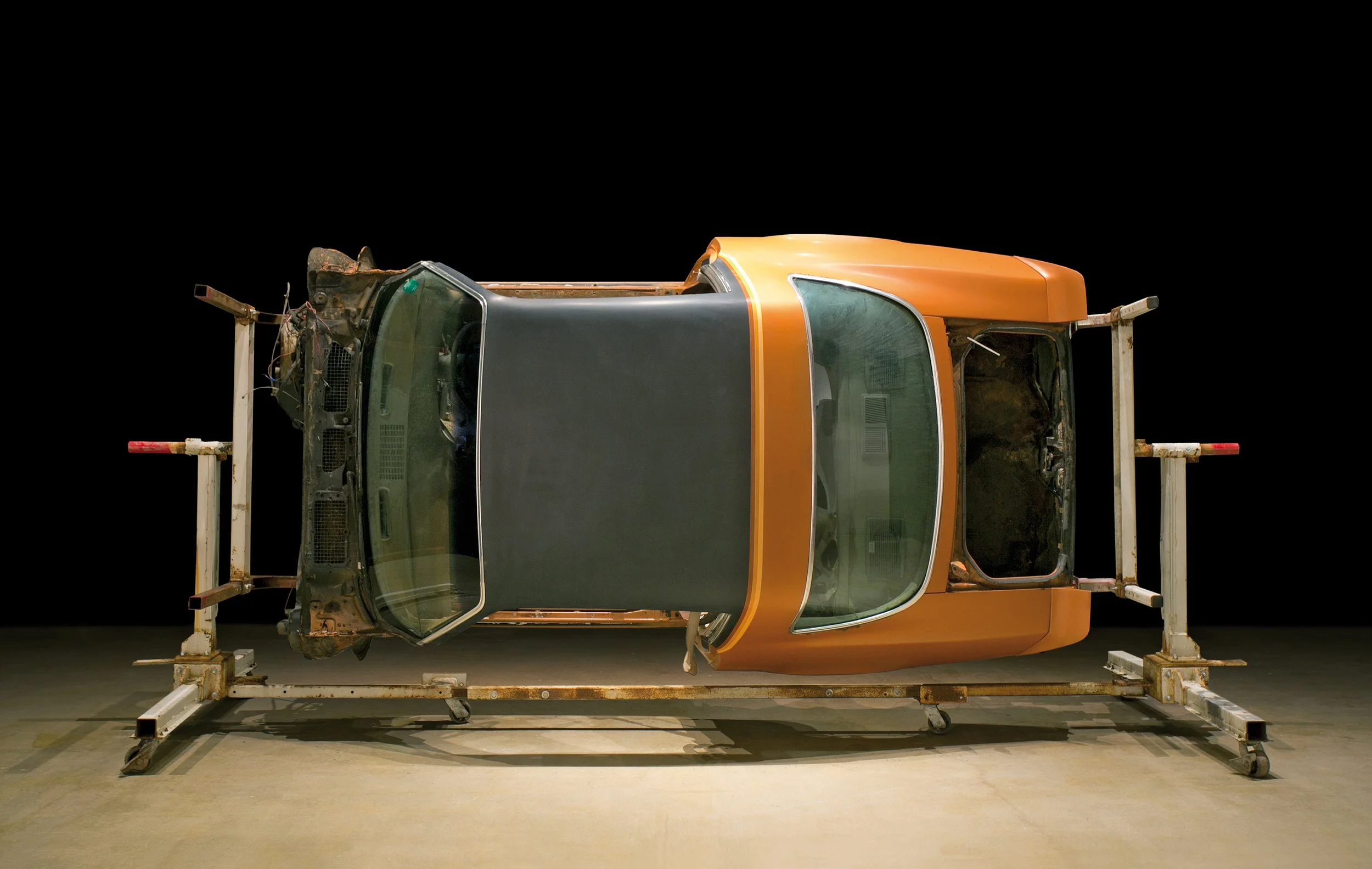 An upright orange and black vehicle cabin mounted on a metal frame with wheels, set against a black background.