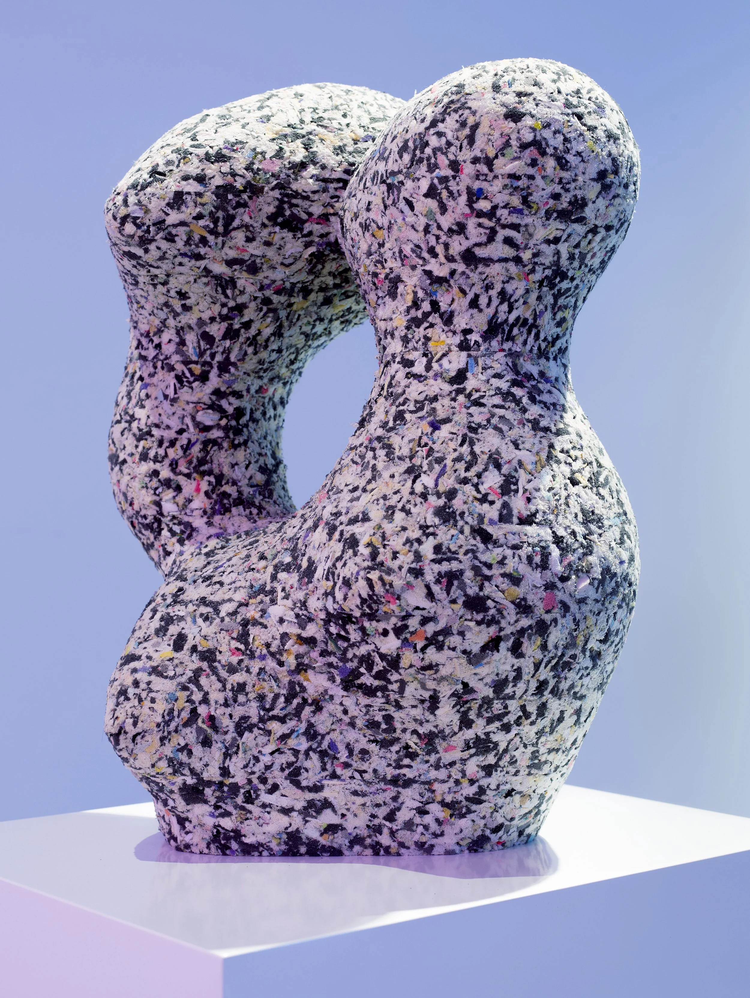 A large, abstract sculpture made of yoga blocks resembling a twisting, elongated form, covered in multicoloured speckles, against a clear blue sky background.