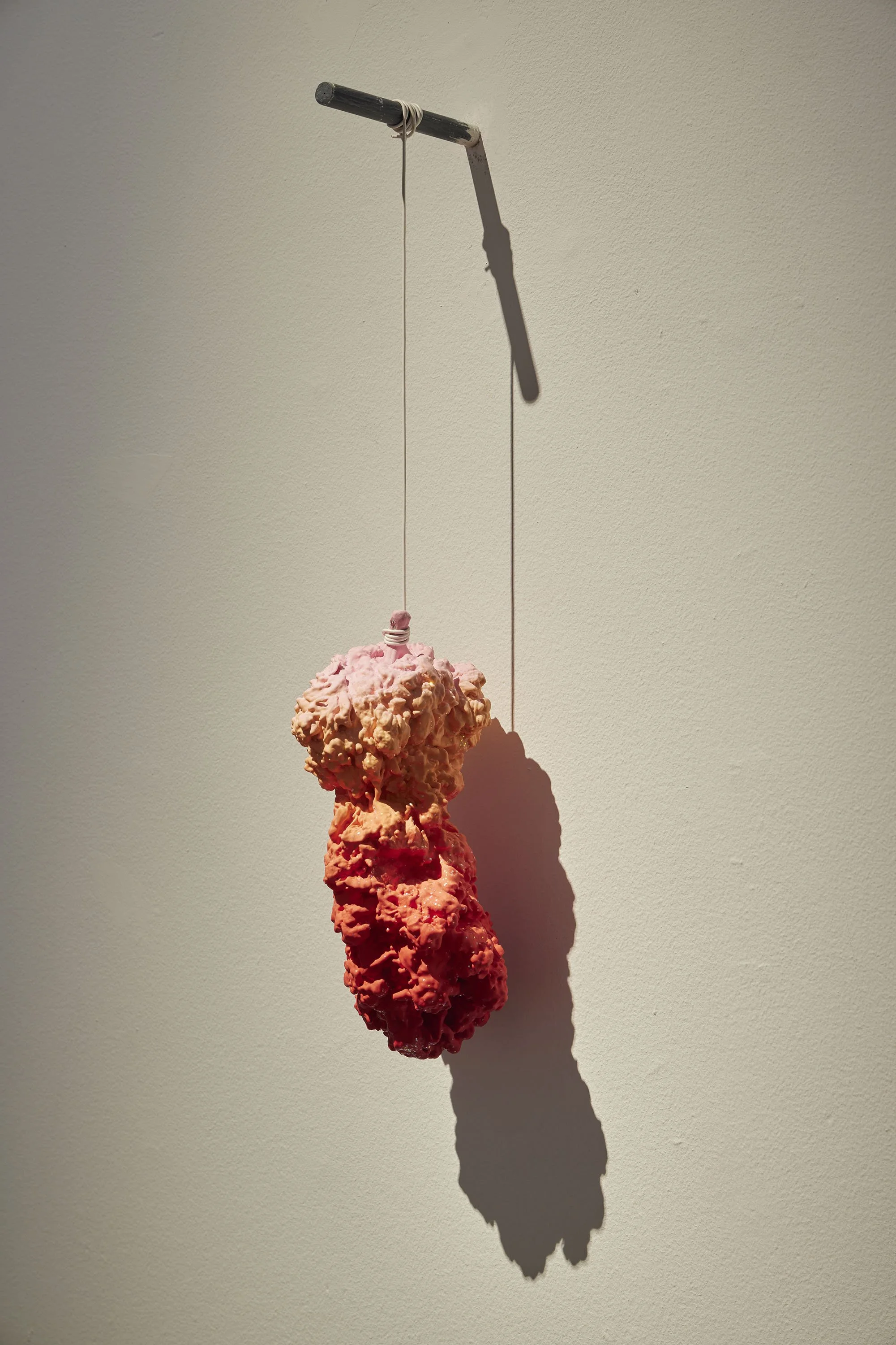 A sculpture of a pinkish-orange marijuana bud hanging from a black rod with a white cord in a gallery.