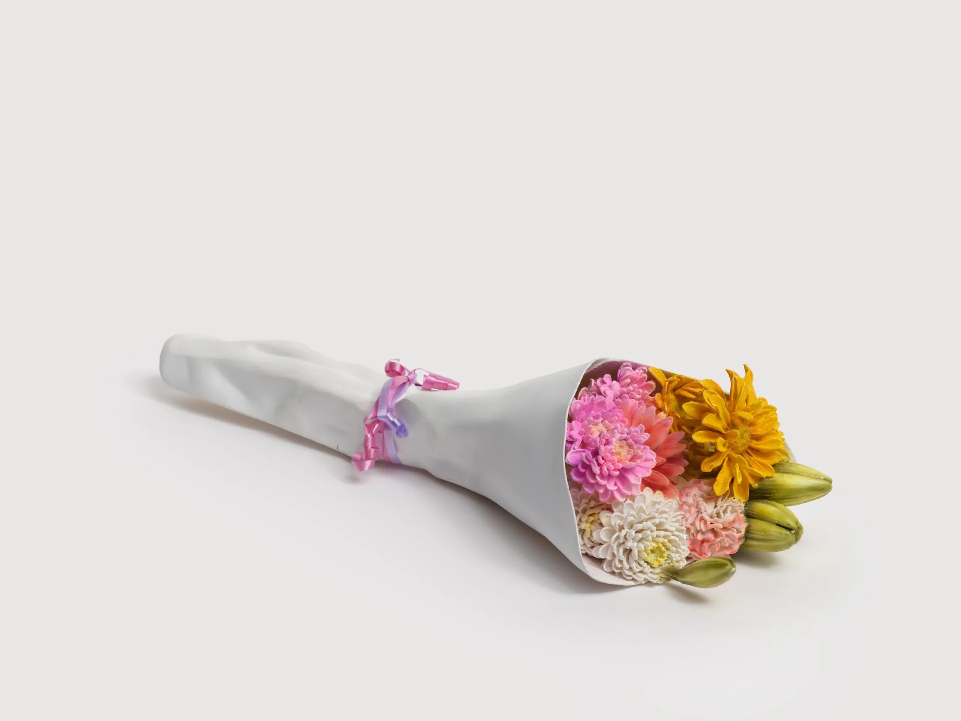 Bouquet of pink, peach, white, yellow, and orange flowers wrapped in white paper with pink and purple ribbon.