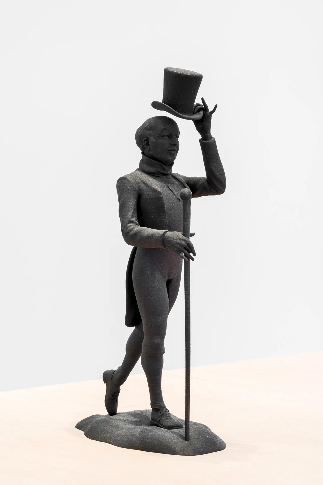 A black statue of a man in a top hat, standing and holding the brim of his hat, with detailed clothing and a walking stick.