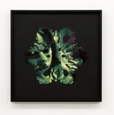 A framed artwork of a Linda Blair from the film The Exorcist, cut into a snowflake creating a green and black butterfly with abstract patterns on a black background