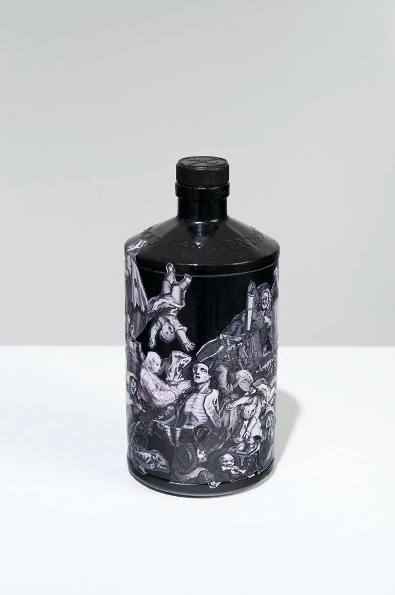 Black bottle with illustrated comic-style characters and scenes on it, placed on a white surface against a plain white background.