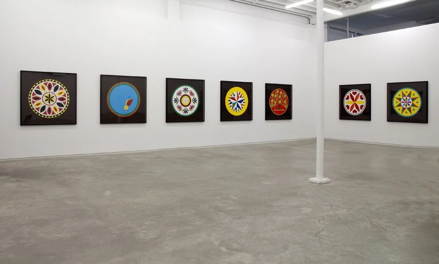 Gallery wall with eight colorful, circular, and symmetrical art pieces displayed in black frames.