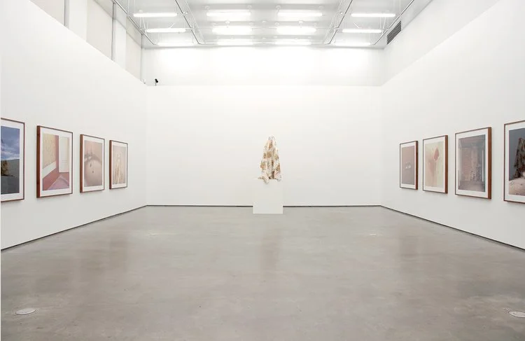 Art gallery with framed pictures on white walls and a sculpture in the center of the room.