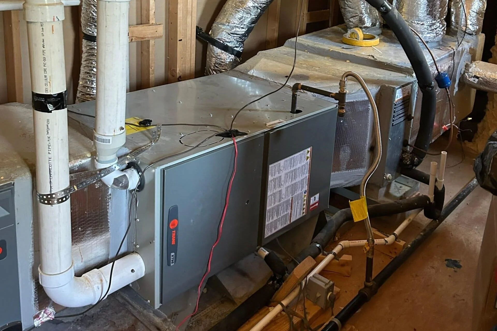 A furnace or HVAC system installed in an unfinished basement with exposed wooden framing and ductwork.