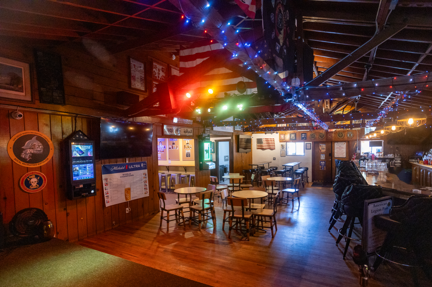 Interior of the American Legion's "Club 416", a bar decorated with holiday string lights, American flags, and sports memorabilia, with tables, chairs, and a bar counter.