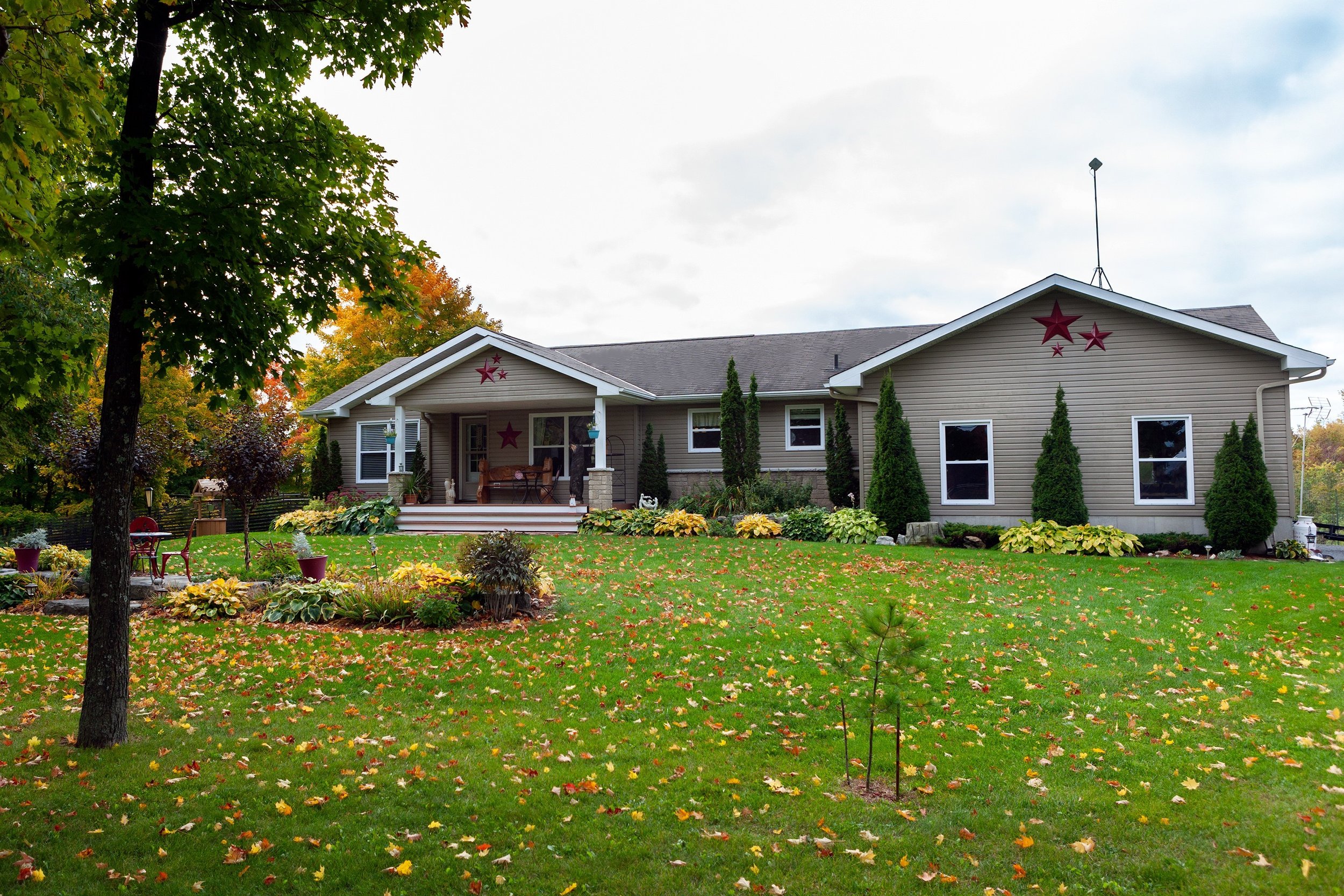 A country bungalow with a large covered porch & entryway. A well landscaped front yard with beautiful flower beds surrounded by trees and fall foliage.