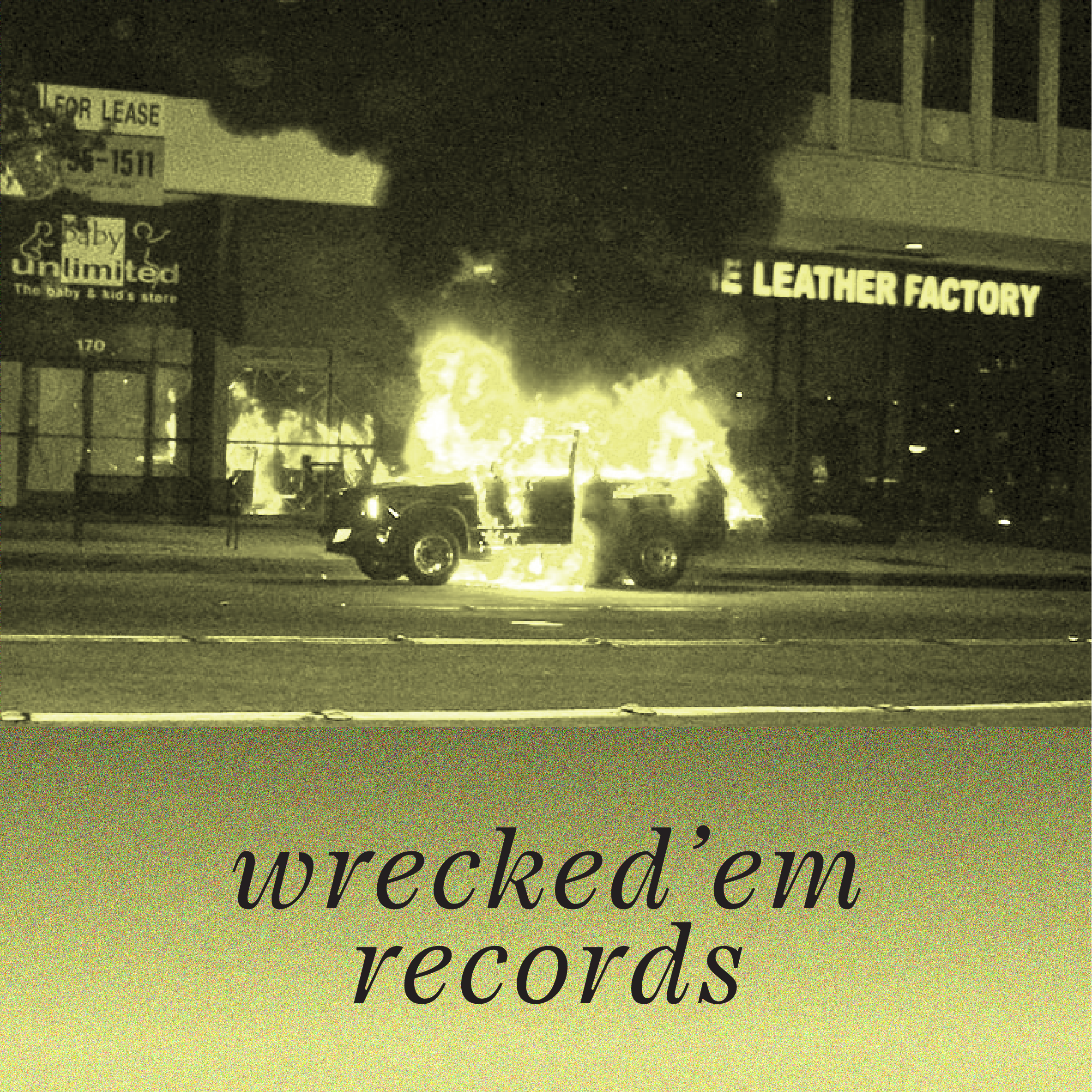 Nighttime street scene showing a car fire with bright flames and smoke, alongside illuminated store signs for 'For Lease' and 'Leather Factory'. Part of a sign with the word 'wrecked' is visible at the bottom.