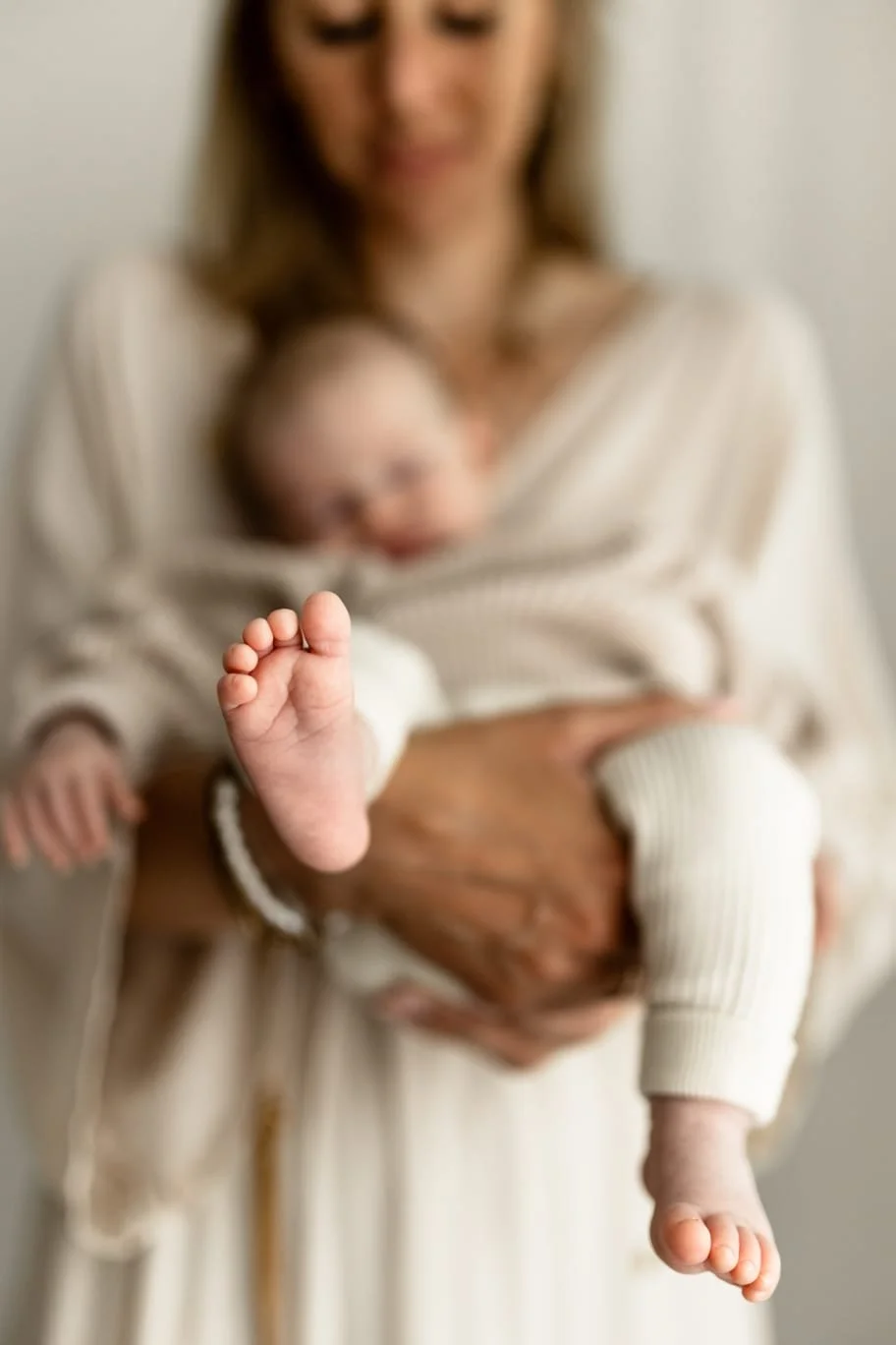 Nahaufnahme eines kleinen Fußes eines Babys, das an einer Mutter sitzt