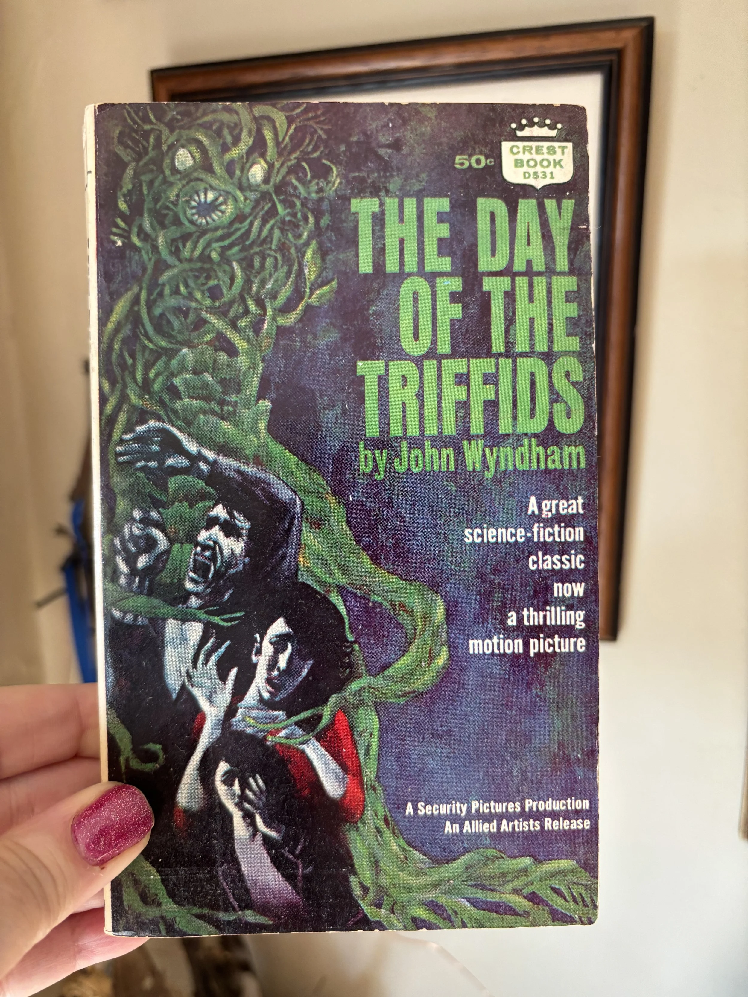 Vintage science fiction book cover titled 'The Day of the Triffids' by John Wyndham, featuring an illustration of a woman with elaborate hair and a man, with a dark and eerie background.