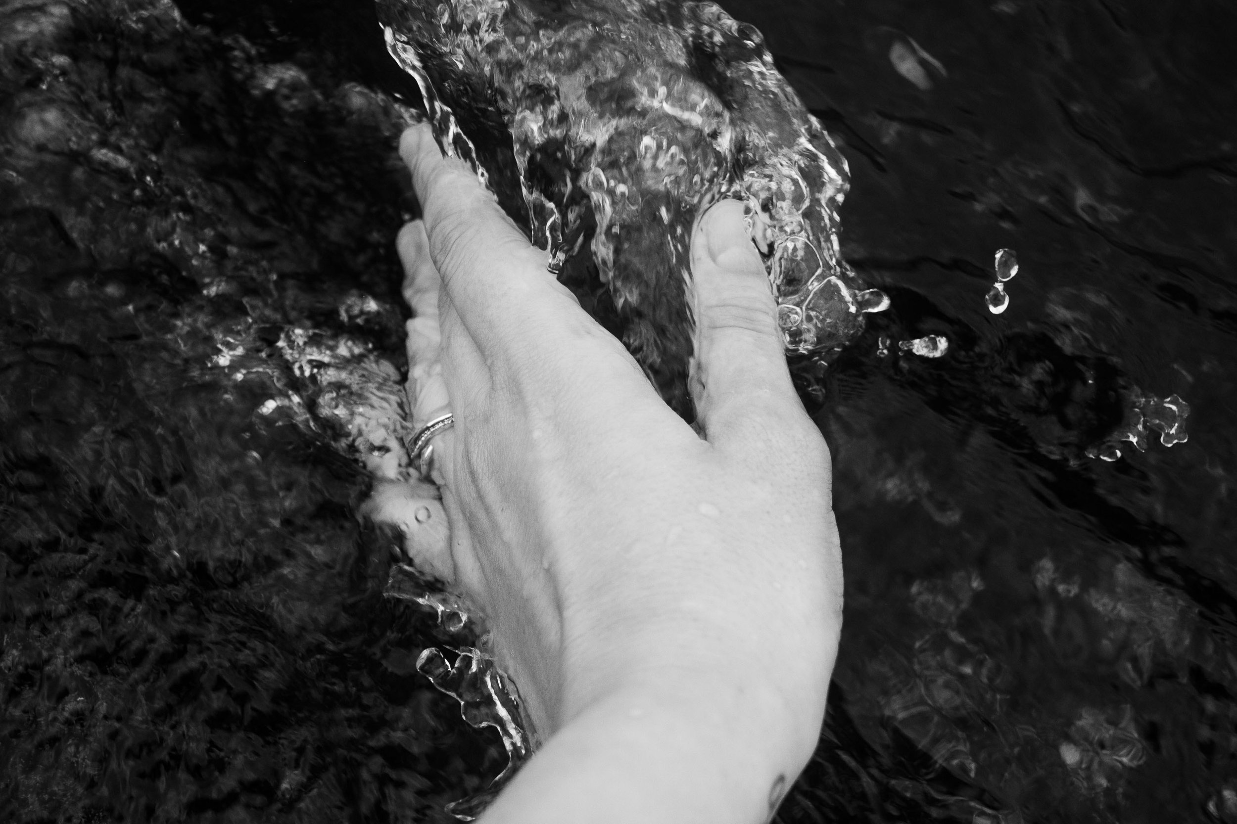 A hand reaches into flowing water.