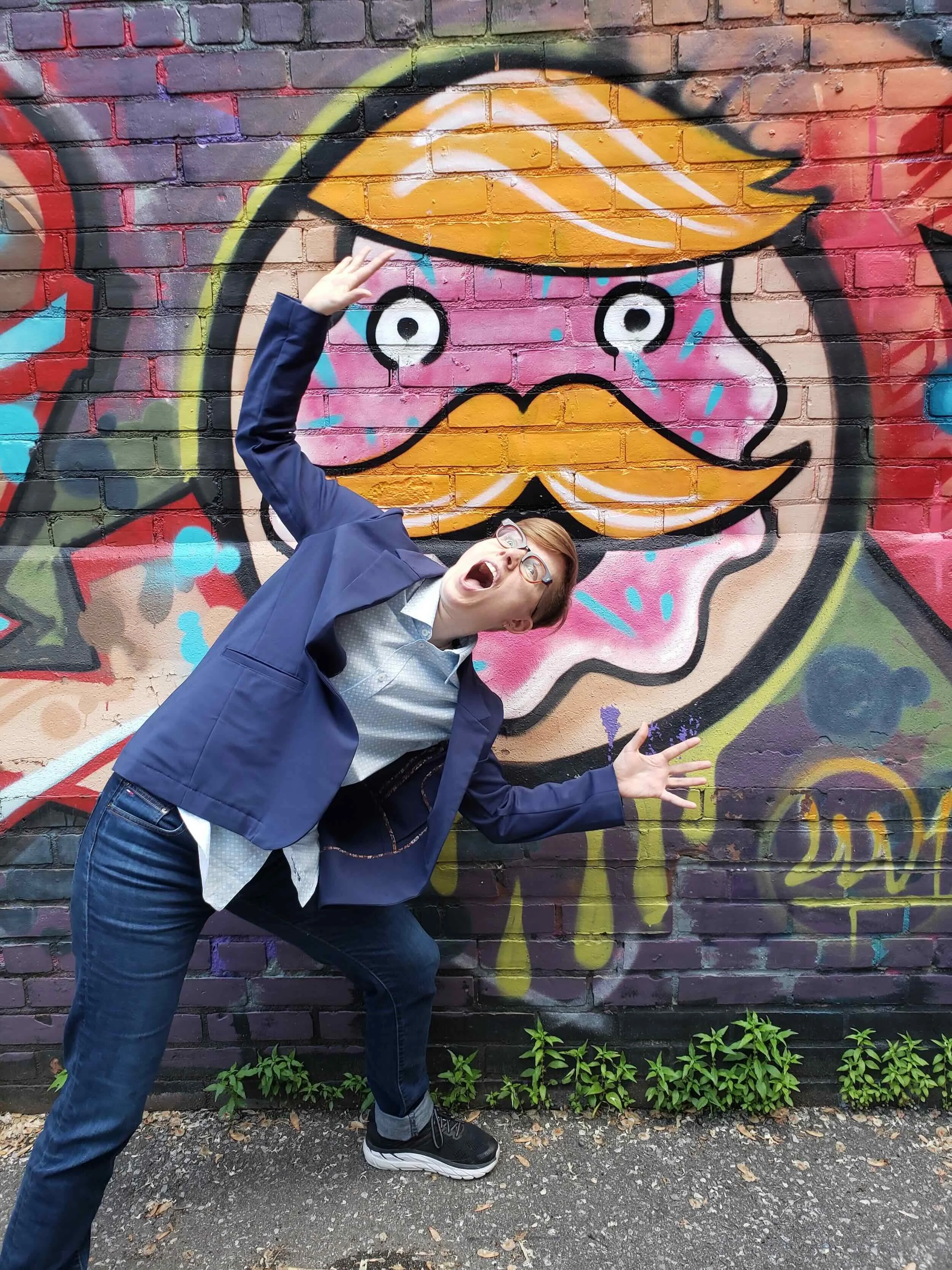 Ezra playfully pretends to be eaten by a colourful graffiti mural of a wide-eyed doughnut face, arms flung wide in mock alarm.