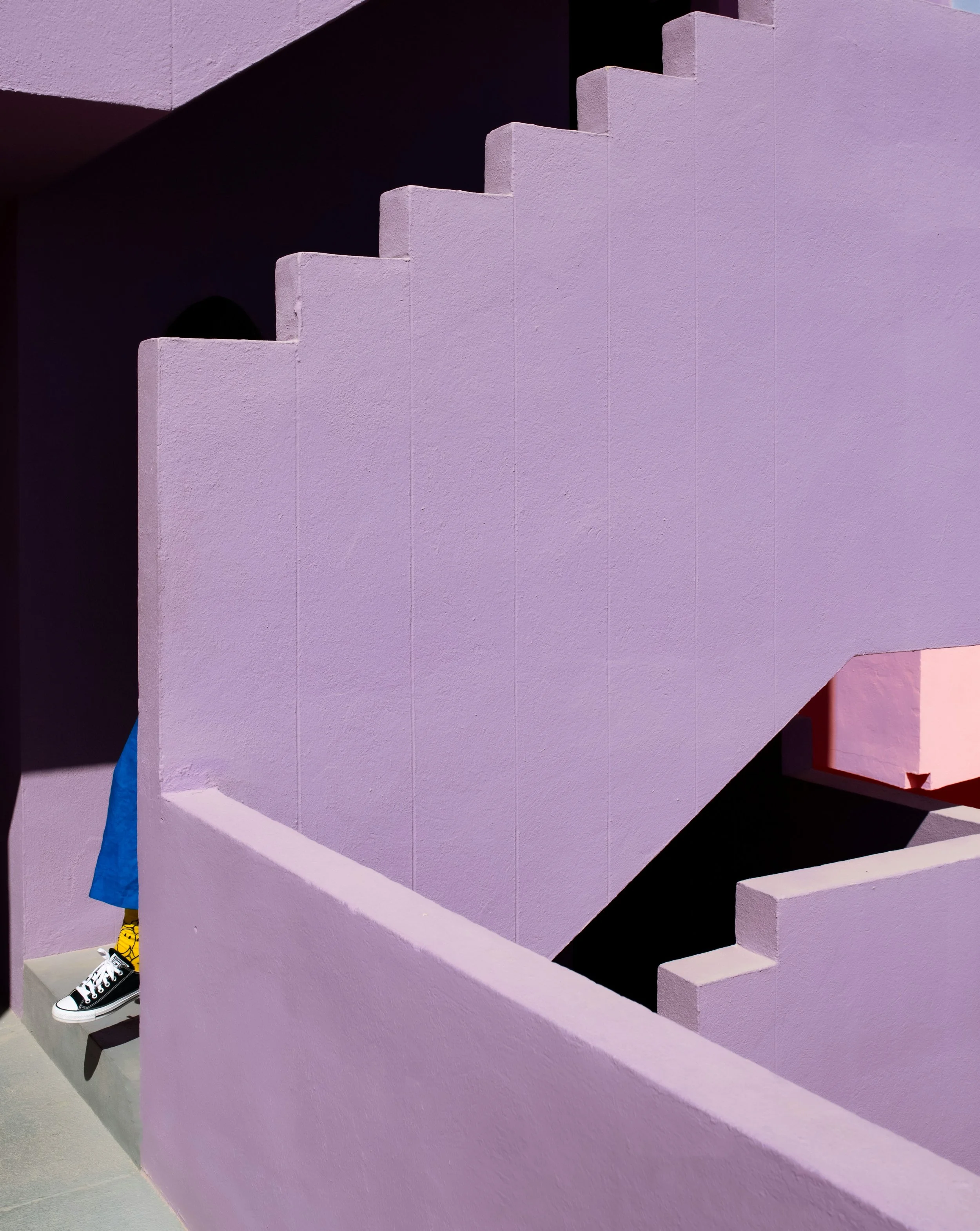 The foot and leg of a person in bright clothing is emerging from behind intersecting lavender walls and steps, suggesting emerging from aspects of sexuality that could feel like a maze.