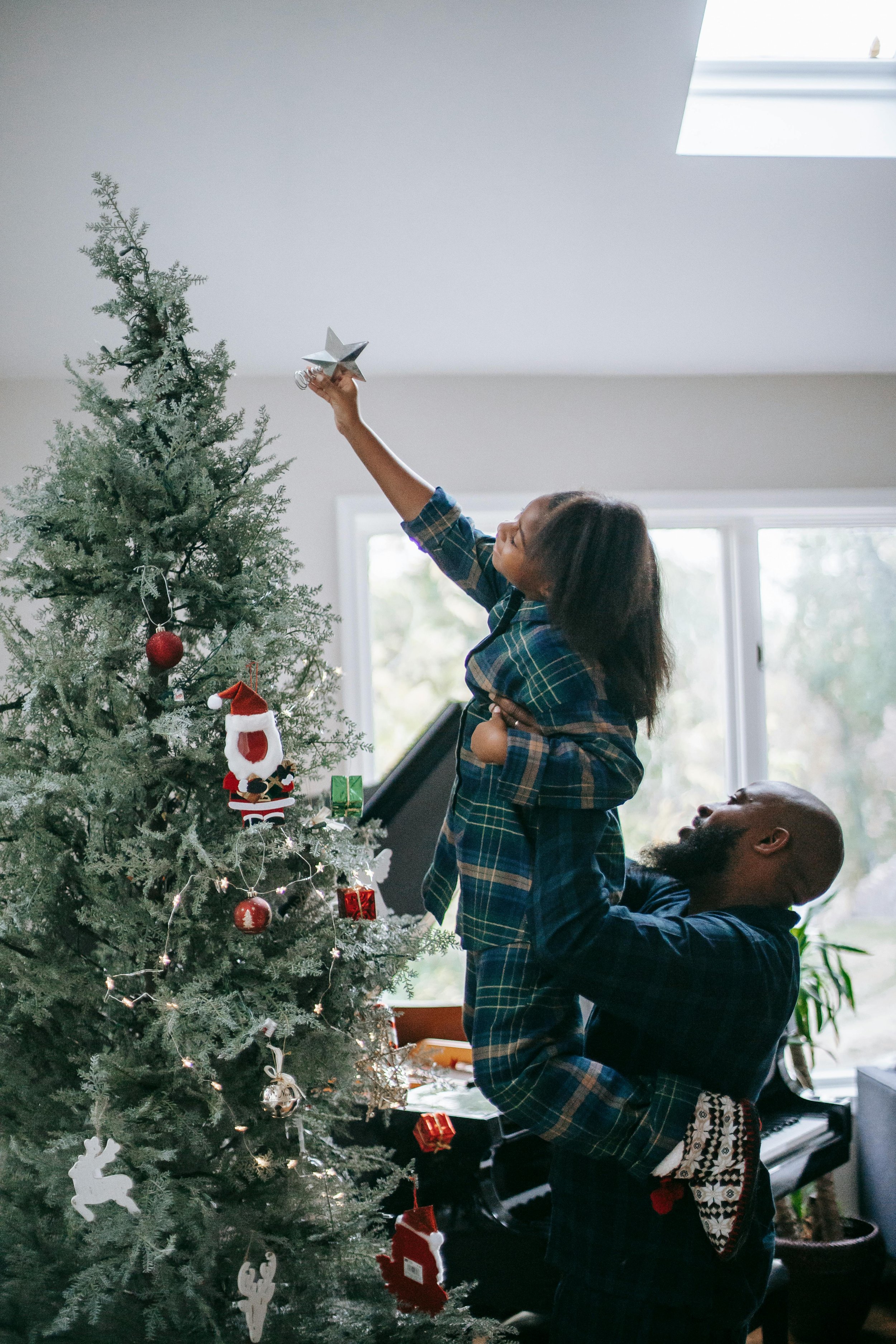 A parent holds their child up to decorate a Christmas tree