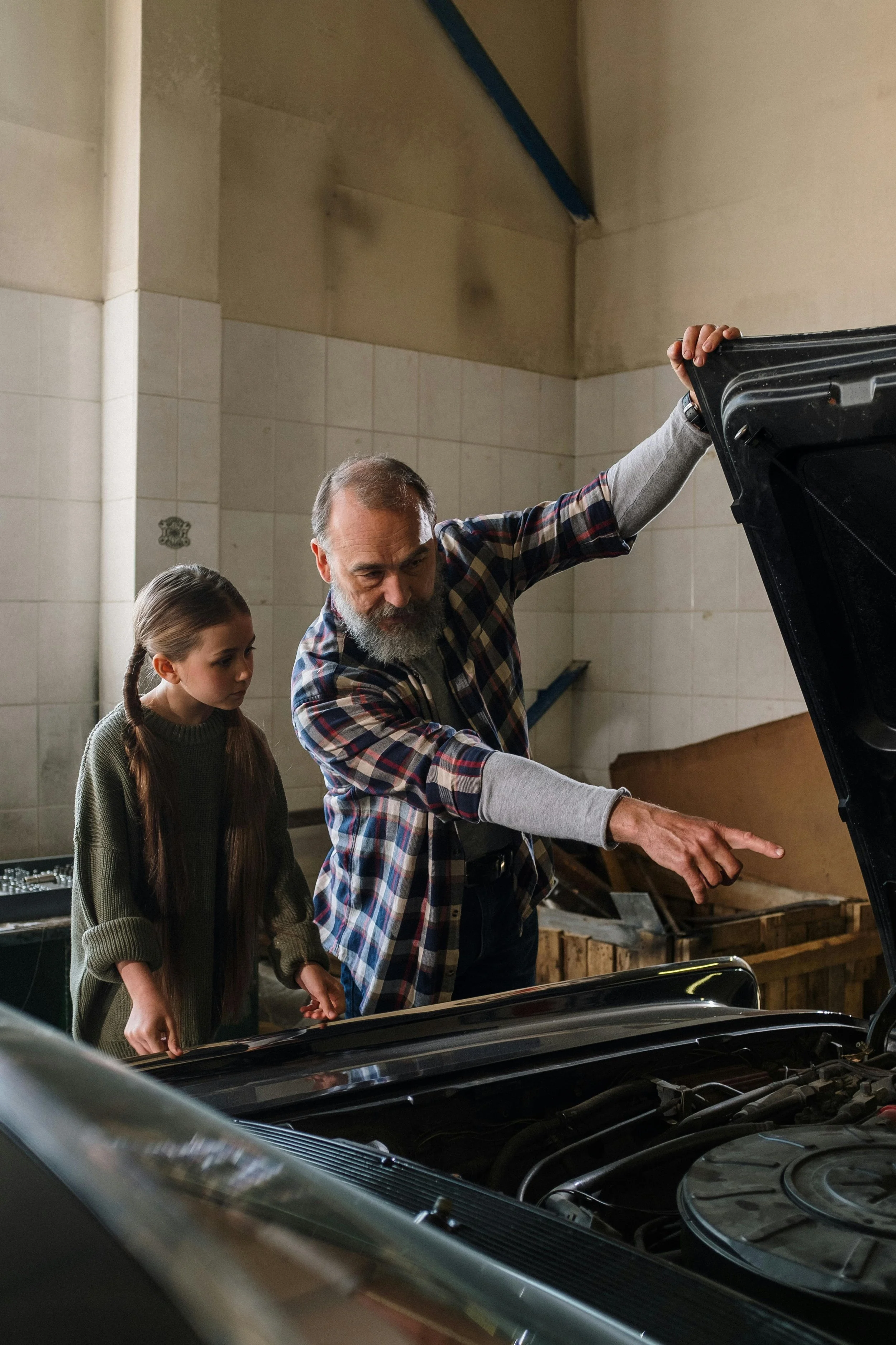 An older man teaches a young girl about cars