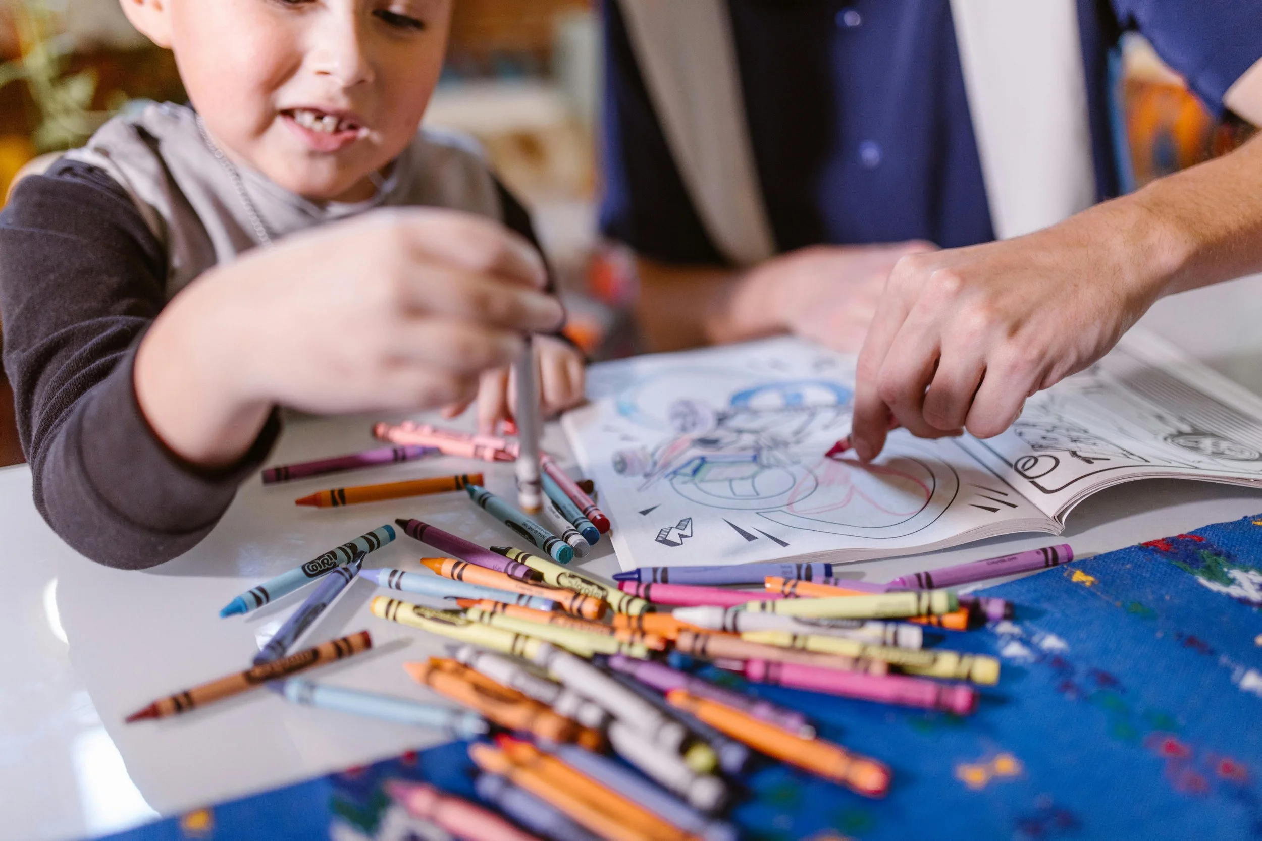 A child and adult color in a coloring book with crayons.