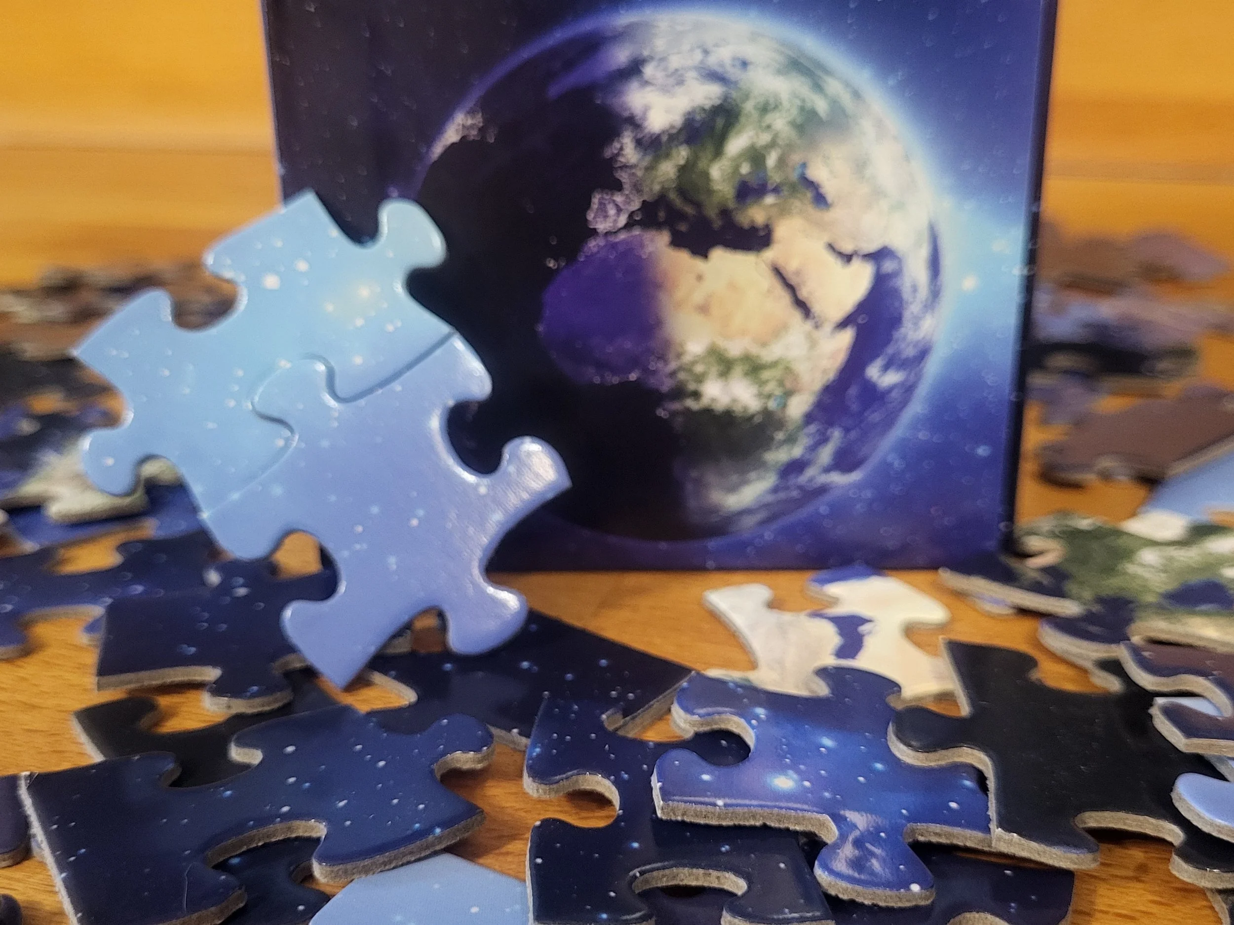 A puzzle with an image of the Earth from space, showing continents and clouds, partially completed and placed on a wooden surface.