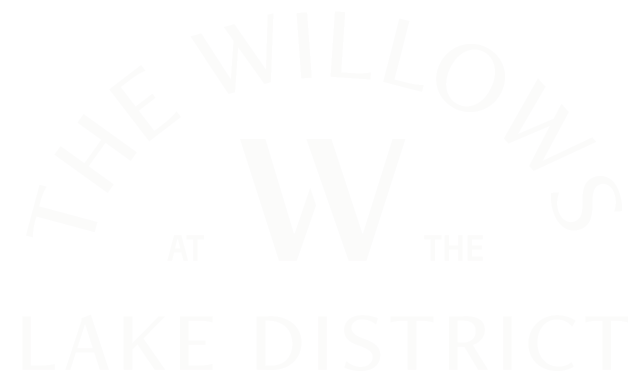 Logo with the text "The Willows at the Lake District" arranged in a circular pattern with a large "W" in the center.