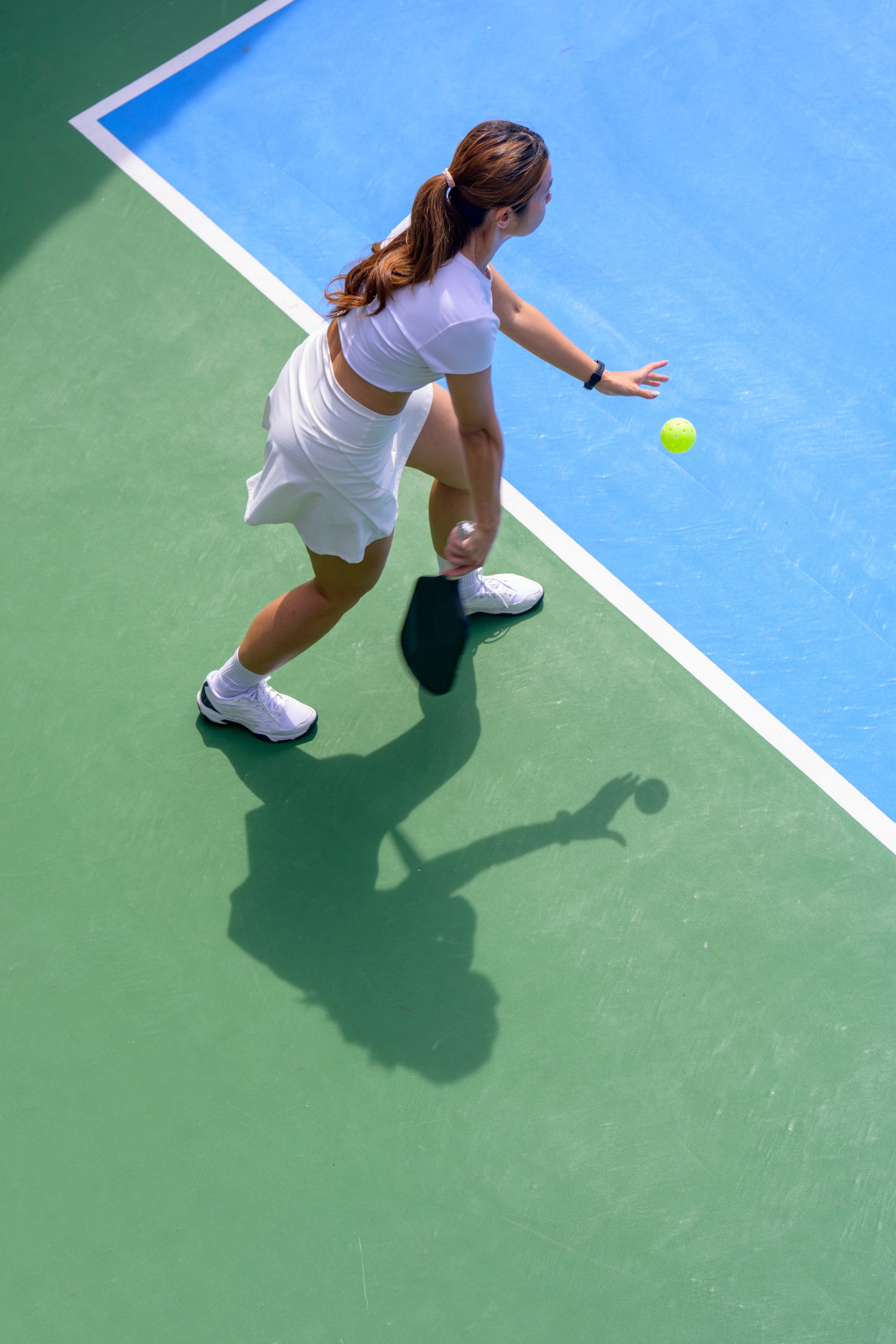 A woman playing pickleball on an indoor court with green and blue surfaces, holding a paddle, preparing to hit a yellow pickleball.