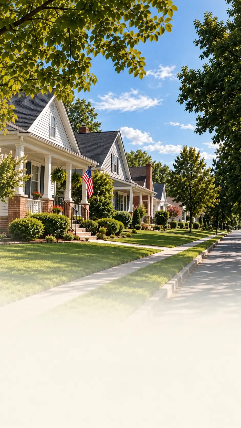 Neighborhood of white houses with front porches, green lawns, trees, and a blue sky with clouds.