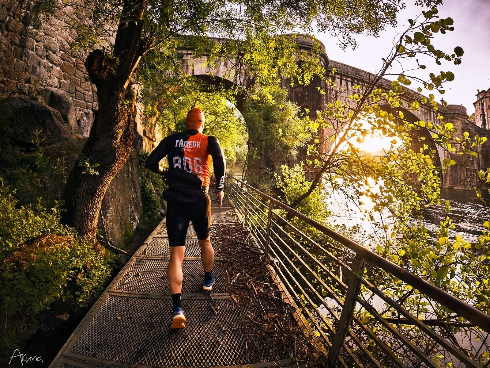 Corredor de bicicleta na ponte com árvores verdes ao lado, rio ao lado e luz do pôr do sol.