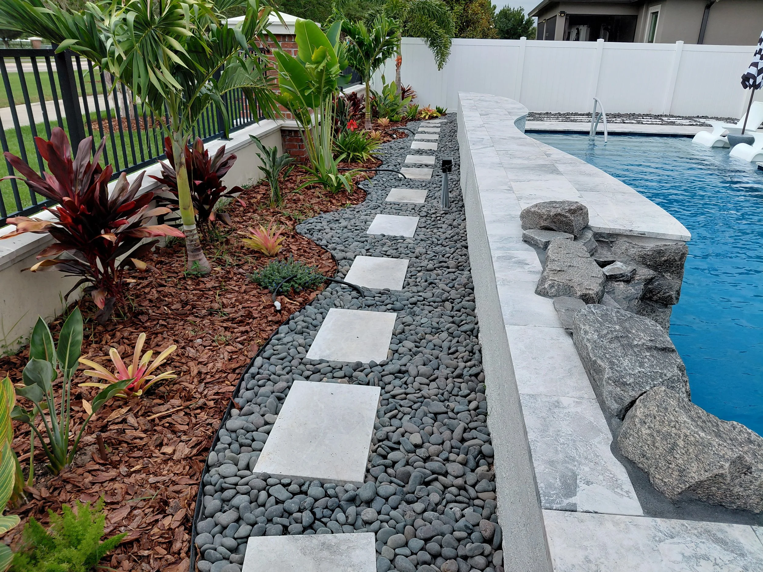 Riverview, FL-Pool-side landscape design featuring travertine step stones, Mexican Beach Rocks, and tropical ornamental plantings. Designed to complement the water's edge.