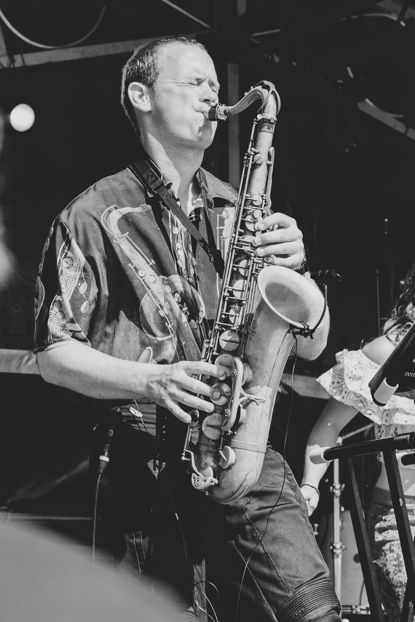 Black and white photo of musician Tim de Vries playing a saxophone in the band Toscans Brew with his eyes closed, wearing a patterned shirt, at SAIL Harlingen 2026.