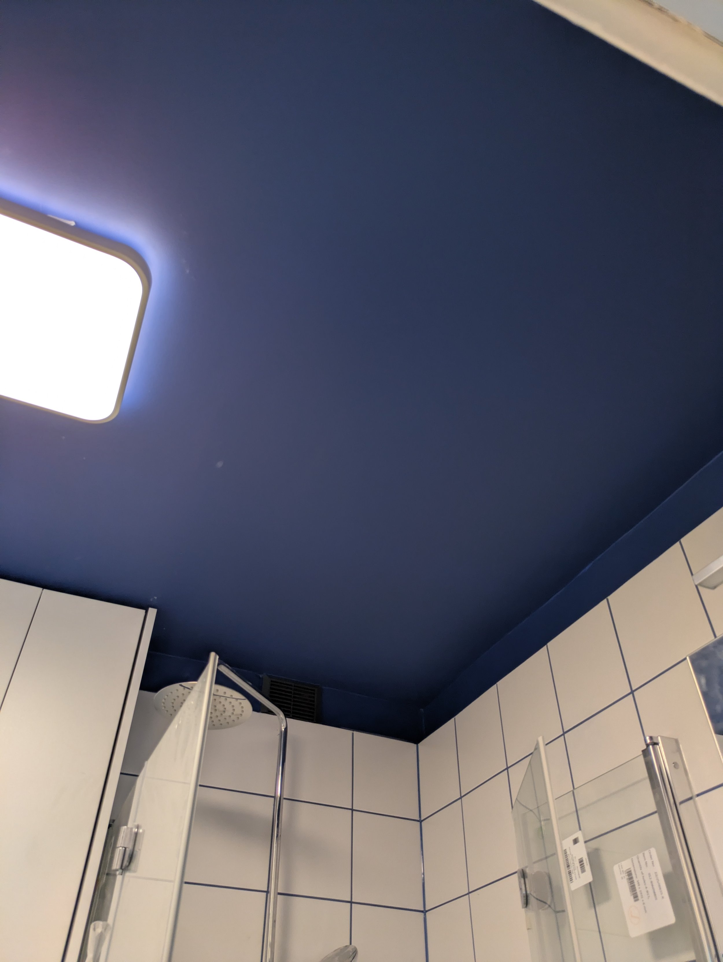Interior view of a bathroom with a white vanity, sink, and faucet, blue painted walls, and white tiled floor showing a vent and partial view of a glass shower door.