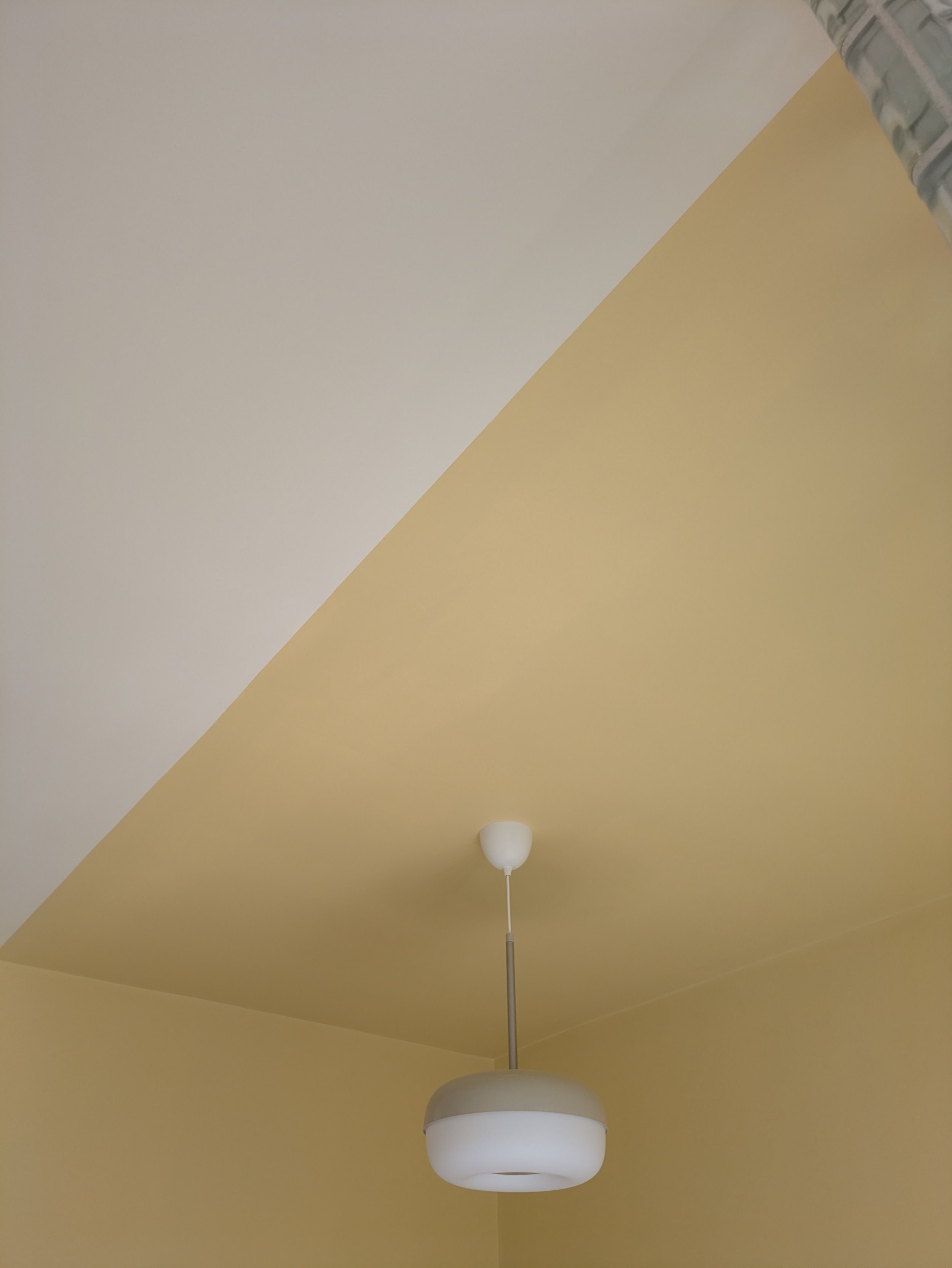 Ceiling-mounted white pendant light fixture with a rounded, layered design, hanging from a white cord on a yellow ceiling.