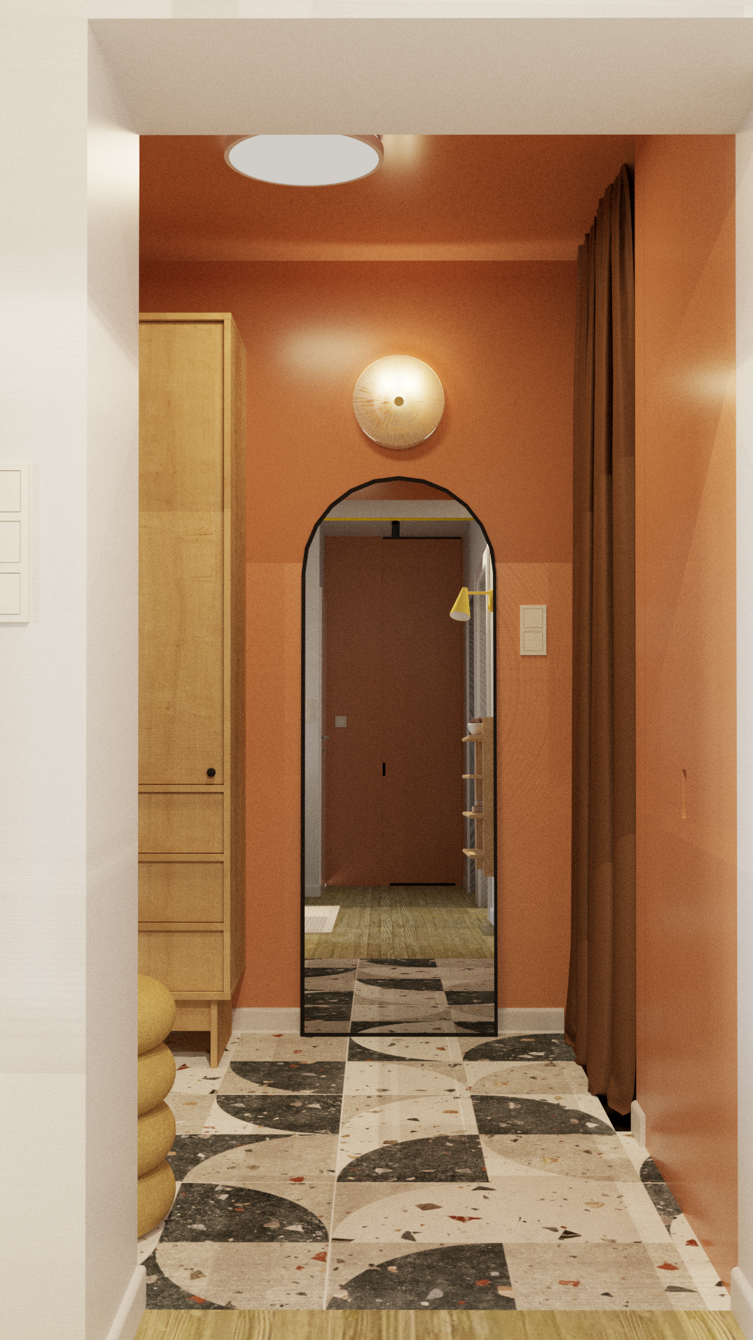 A corridor with a black-framed floor mirror, a peach wall with a circular wall sconce light, a wooden cabinet on the left, and brown curtains on the right. The floor has a patterned black, white, and red tile design.