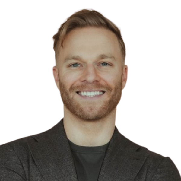 A smiling man with short blonde hair, a beard, wearing a dark blazer over a dark shirt.