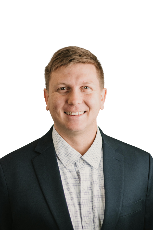 A smiling man wearing a dark blazer and a white collared shirt against a plain background.