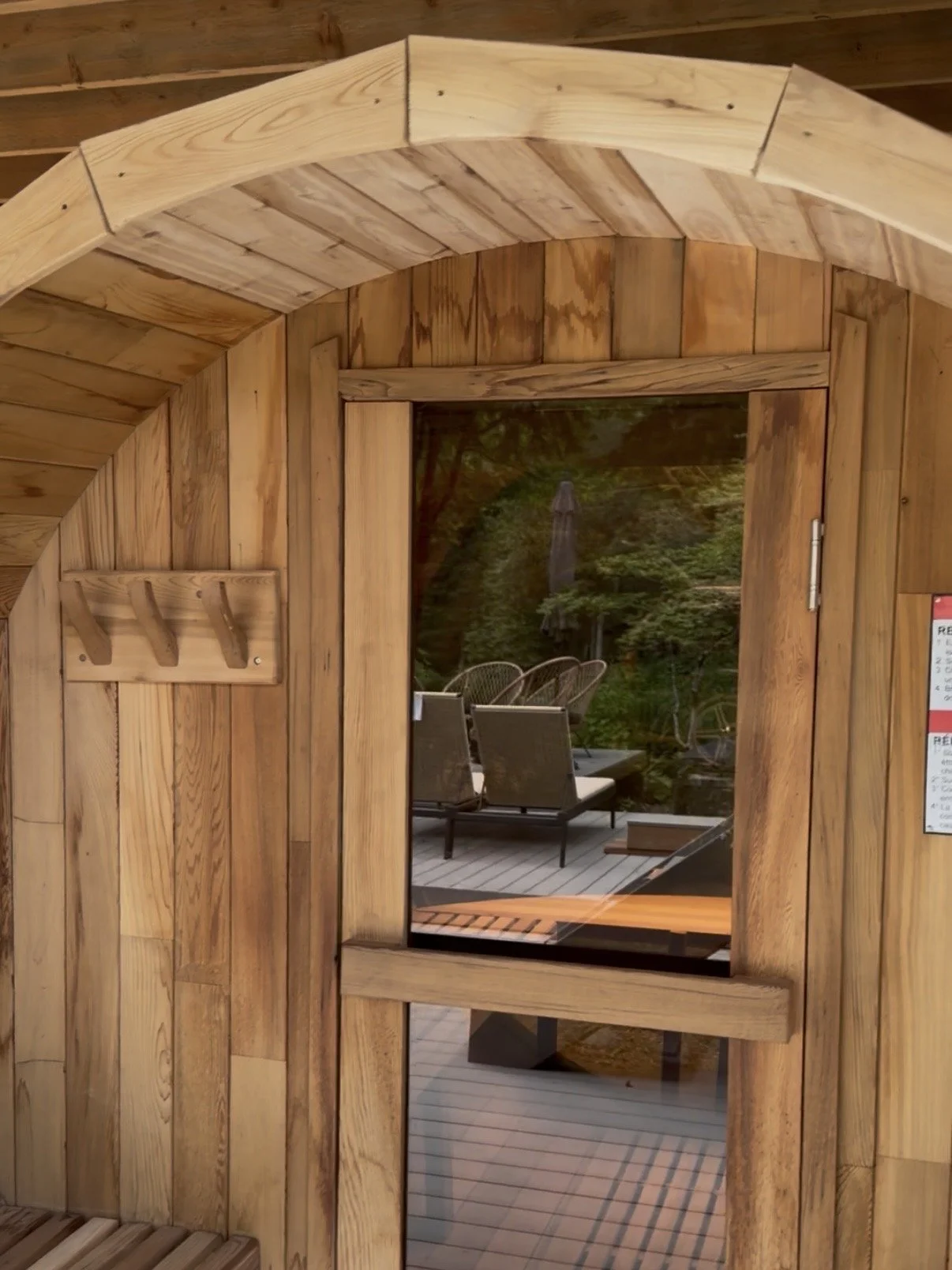 View through a wooden and glass door showing outdoor patio furniture, trees, and a large umbrella in the background.