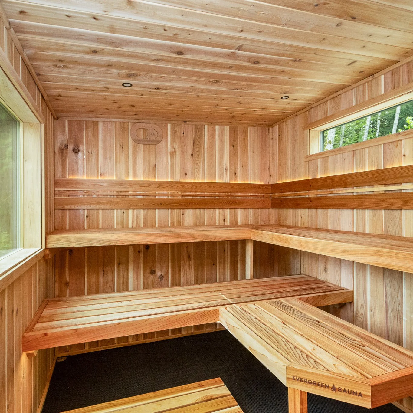 Interior of a wooden sauna with multiple tiered benches and a window showing trees outside.