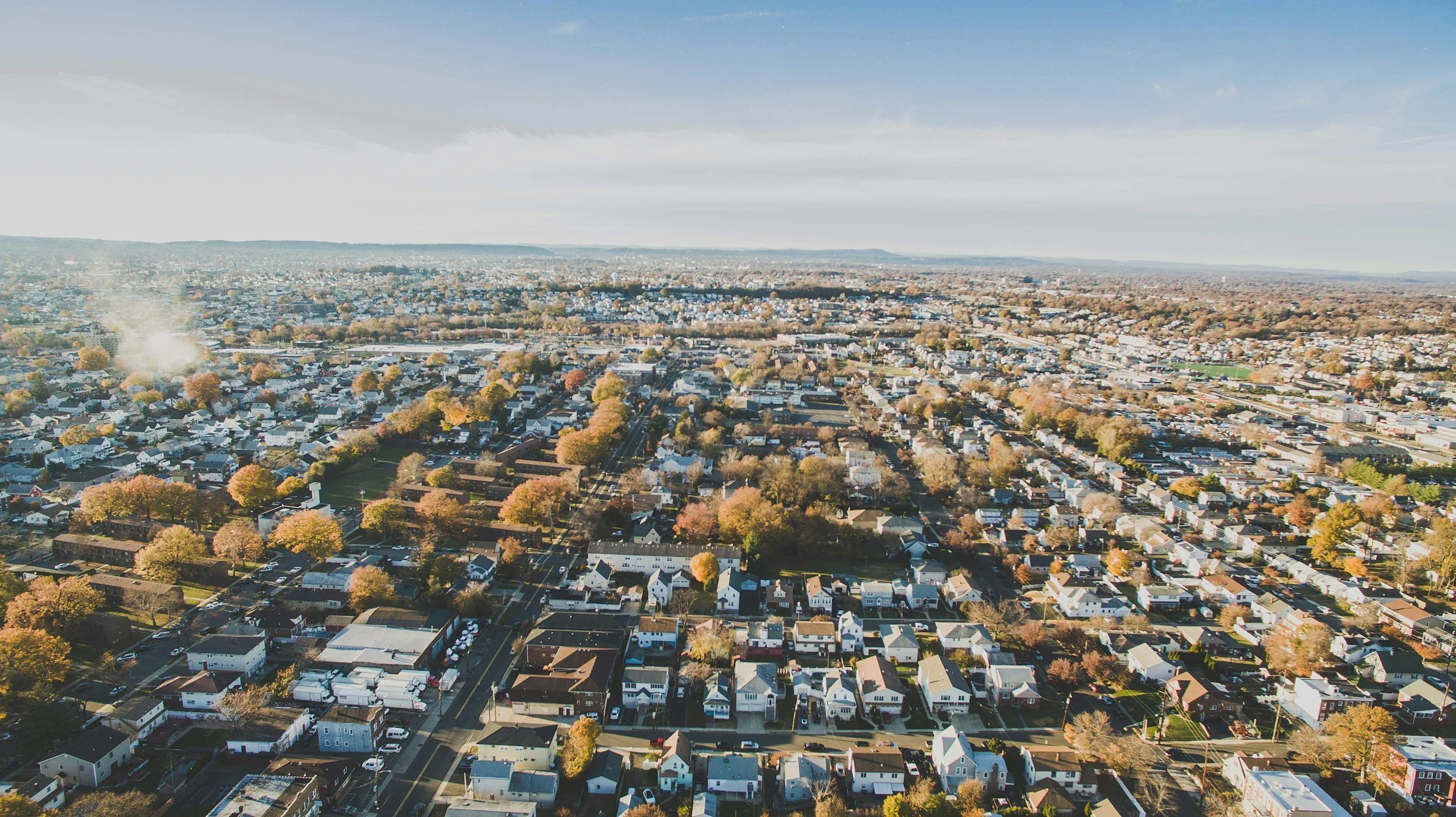 Aerial view of a city with numerous houses, streets, trees showing autumn colors, on a clear day with blue sky.
